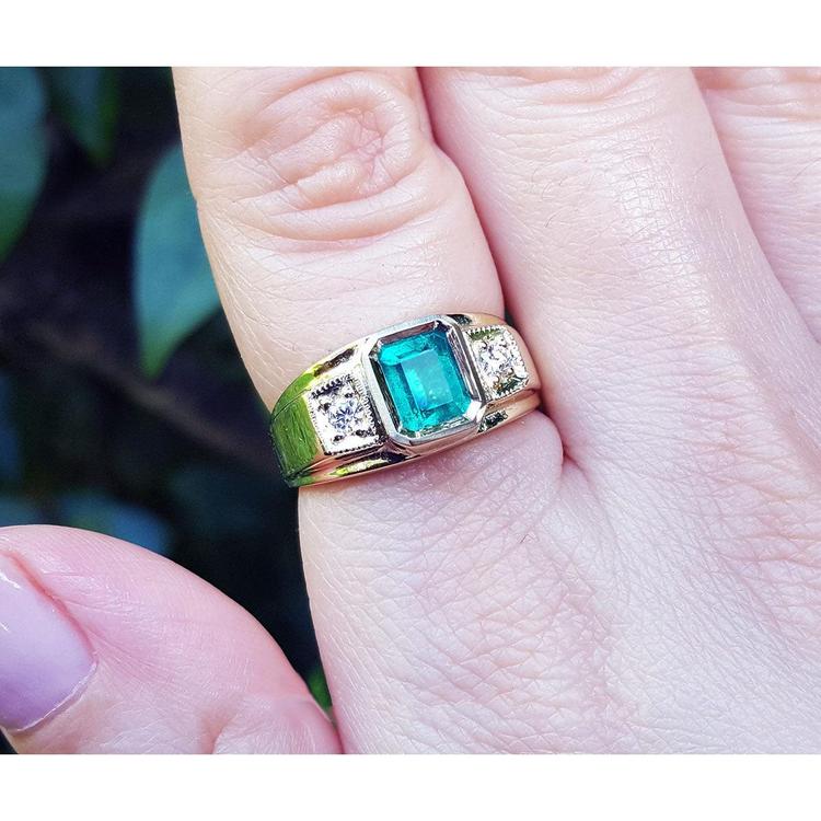Gold ring for man with a natural colombian emerald on a finger against a blurred natural background.