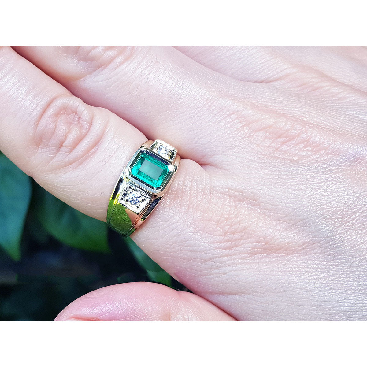 A yellow gold emerald ring for men on a finger against a blurred natural background.