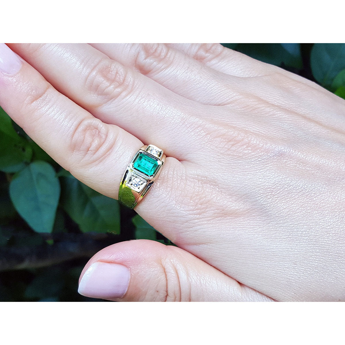 Gold men&#39;s ring with a Muzo colombian emerald on a hand against a natural background.