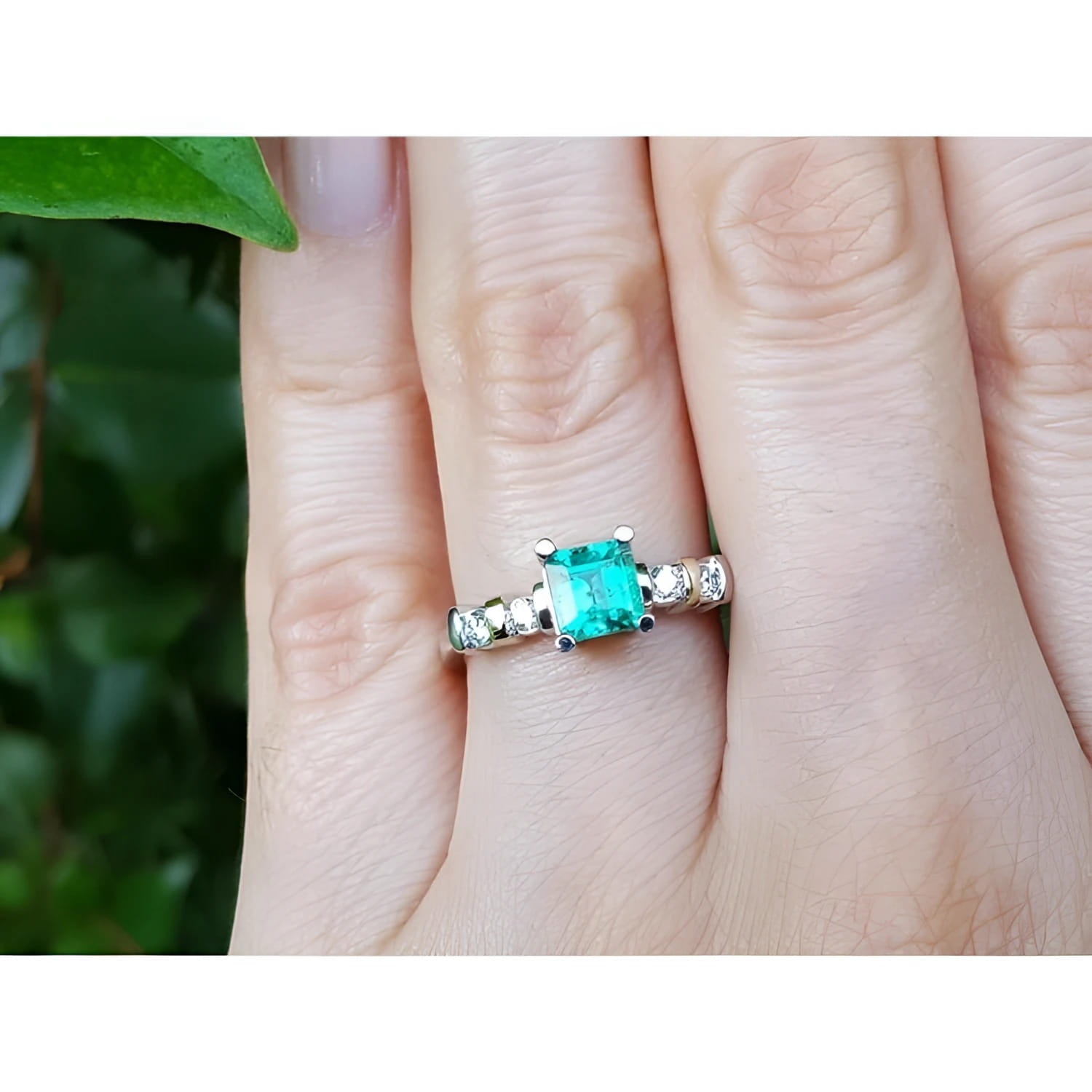 A hand wearing a ring with a natural colombian square emerald with accent diamonds in white gold.