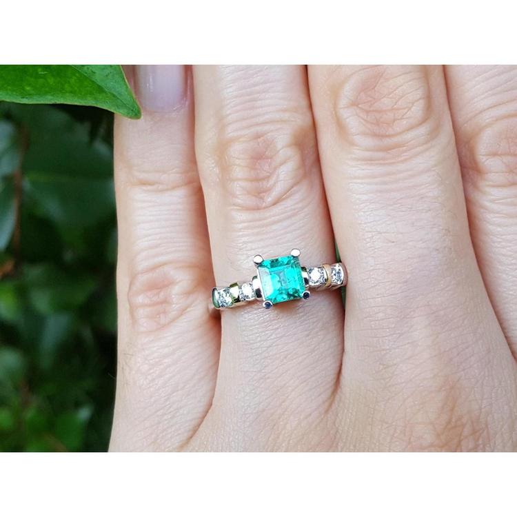 A hand wearing a ring with a natural colombian square emerald with accent diamonds in white gold.