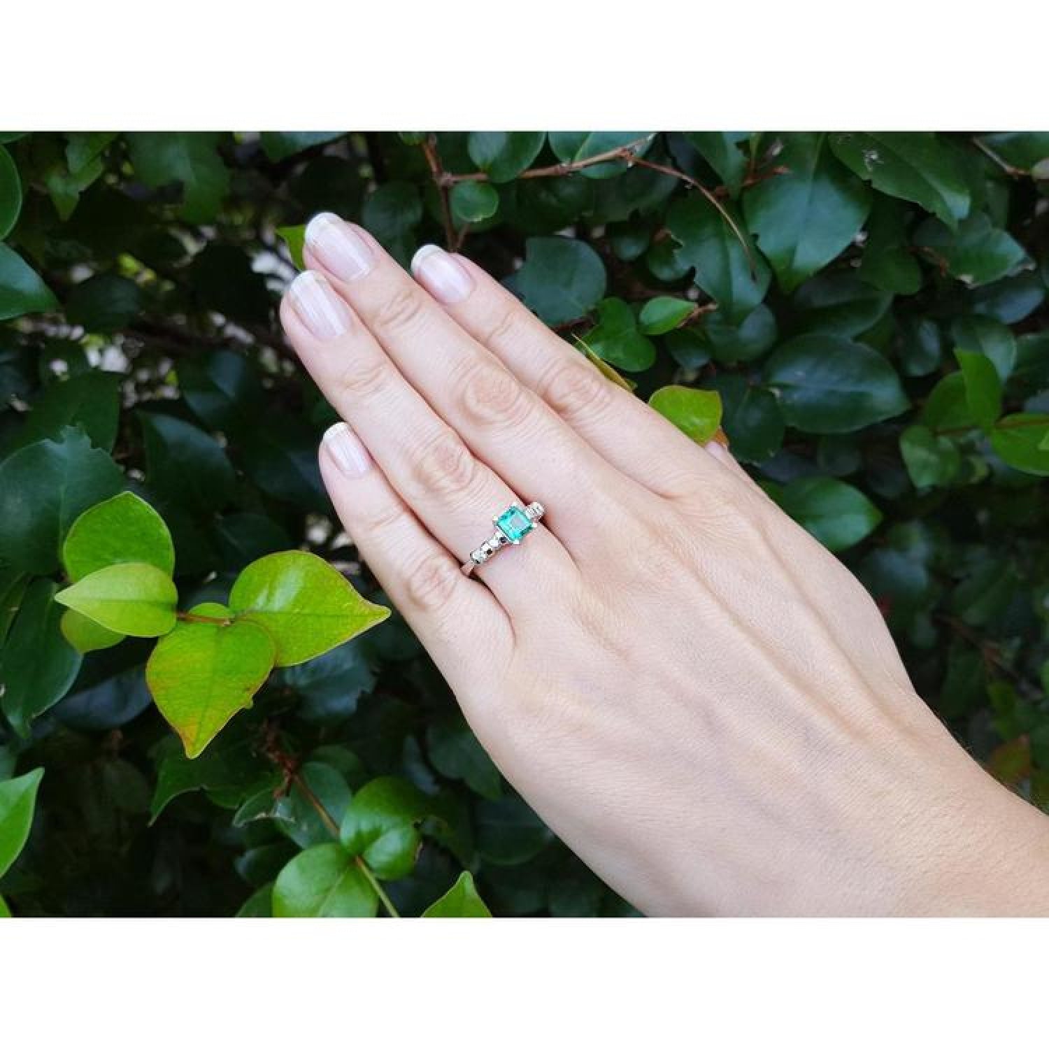 Hand wearing a 14K white gold ring with a square emerald cut Colombian emerald and side diamonds.