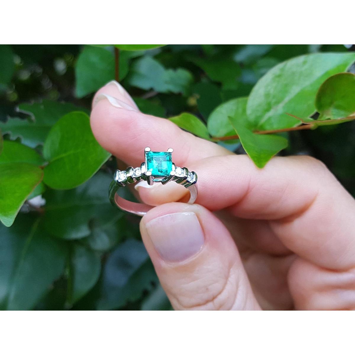 Hand holding a natural emerald ring against a green leafy background.