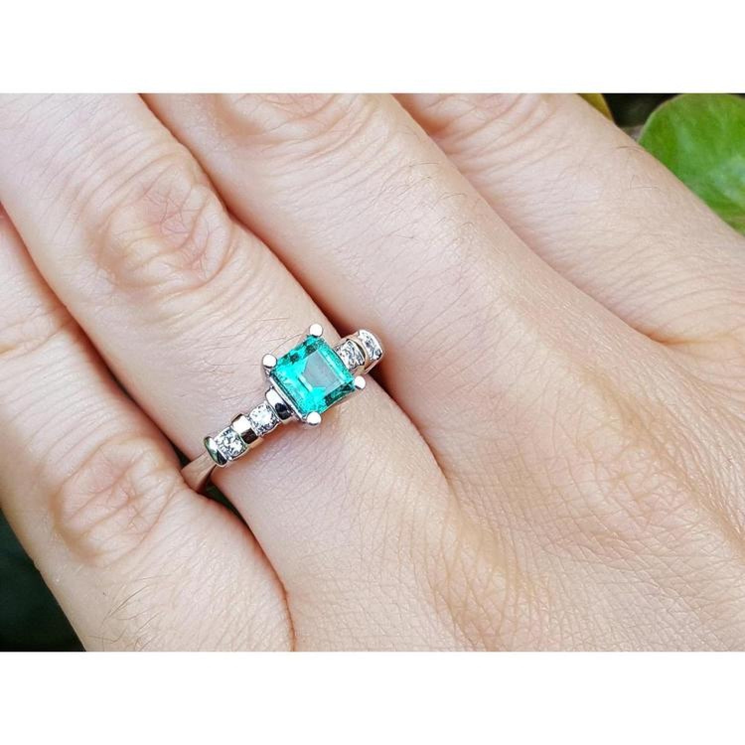 14K white gold ring with a square emerald cut Colombian emerald and sparkling side diamonds on a hand.
