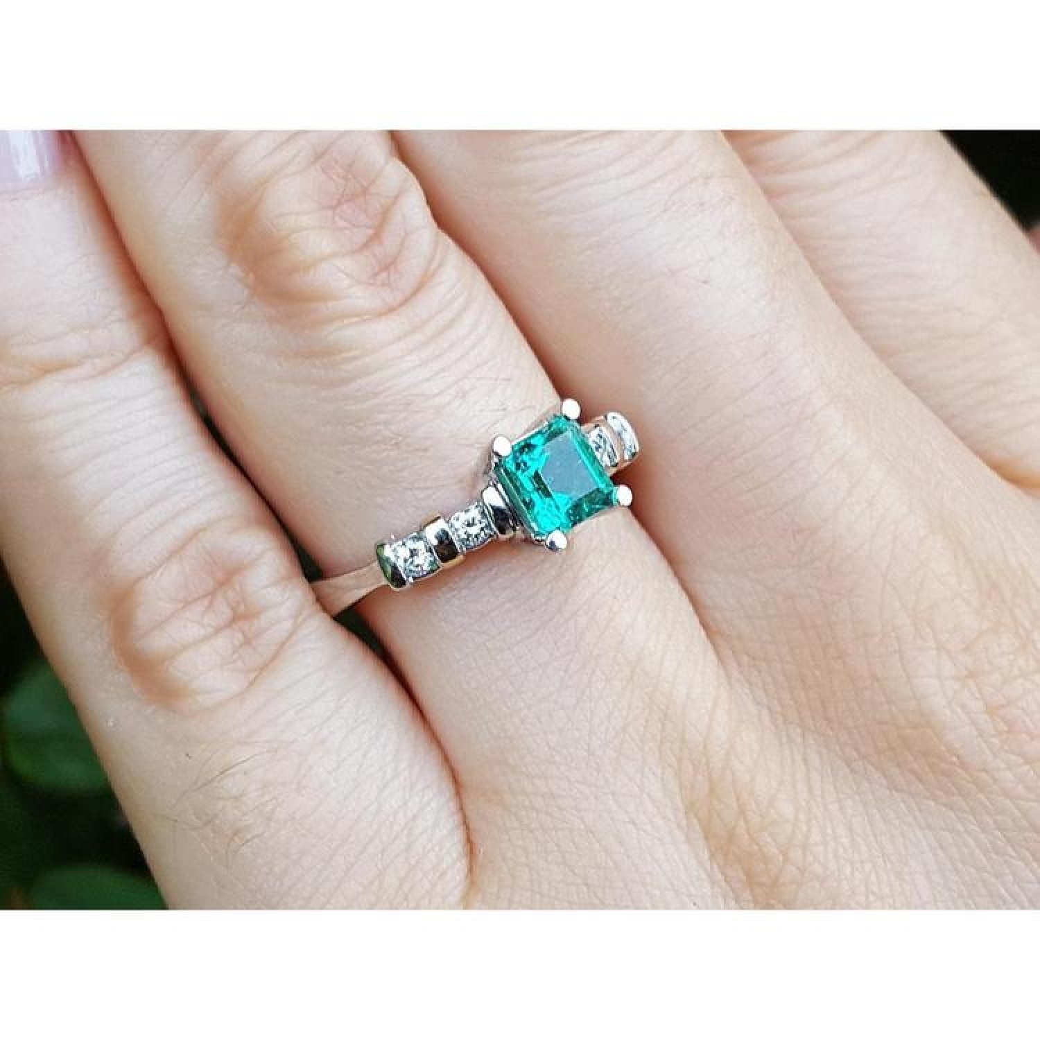 14K white gold ring with a square emerald cut Colombian emerald and side accent diamonds on a hand.