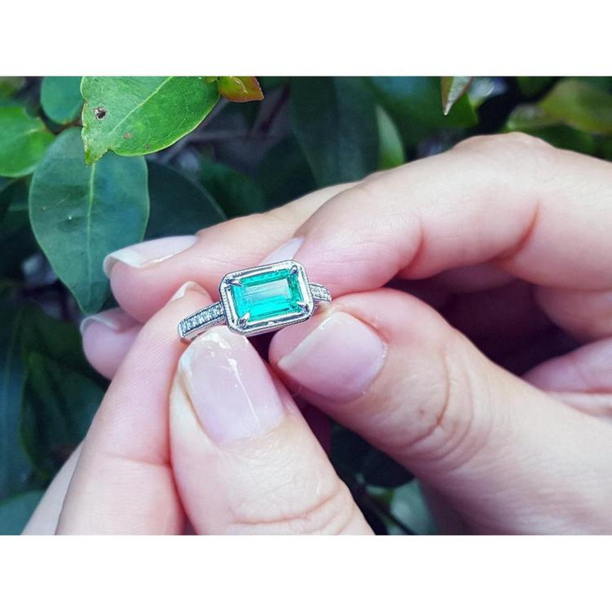 1.21 ct. emerald-cut emerald ring with natural diamonds set in 14K white gold, held by hands.