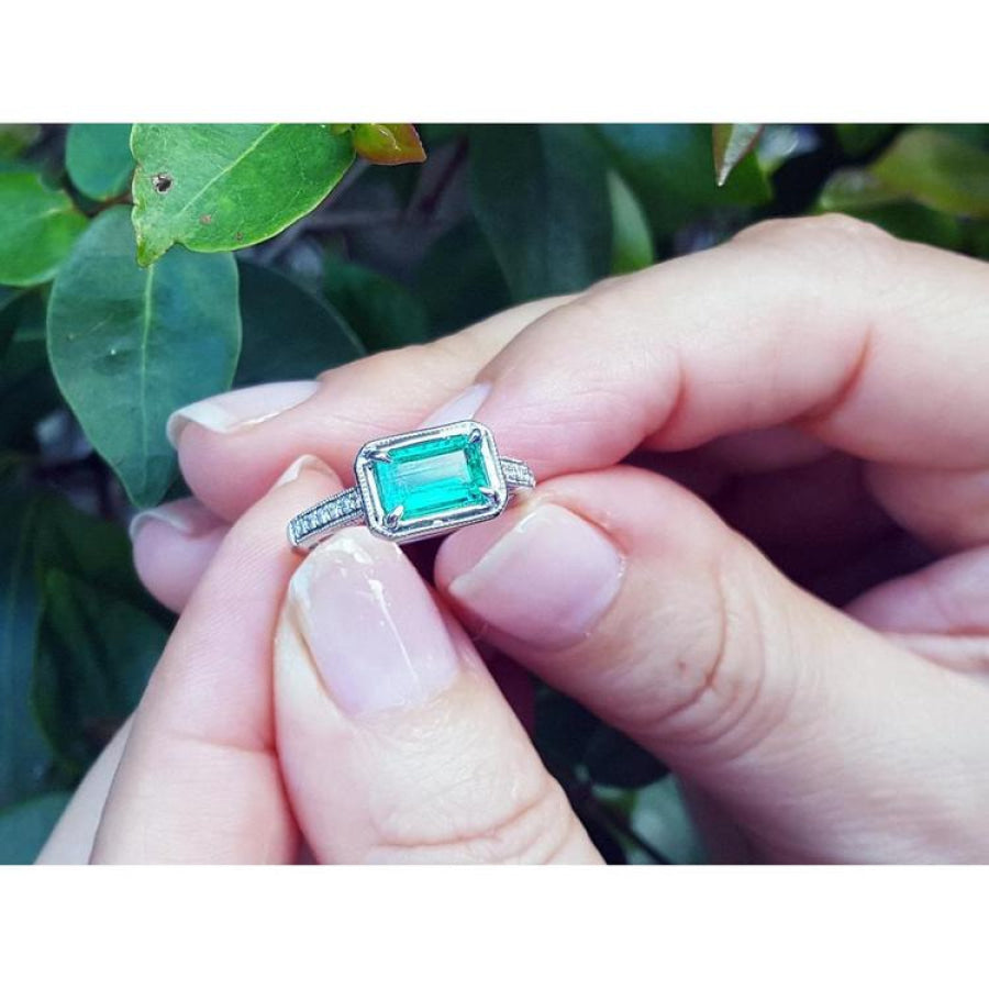 1.21 ct. emerald-cut emerald ring with natural diamonds set in 14K white gold, held by hands.