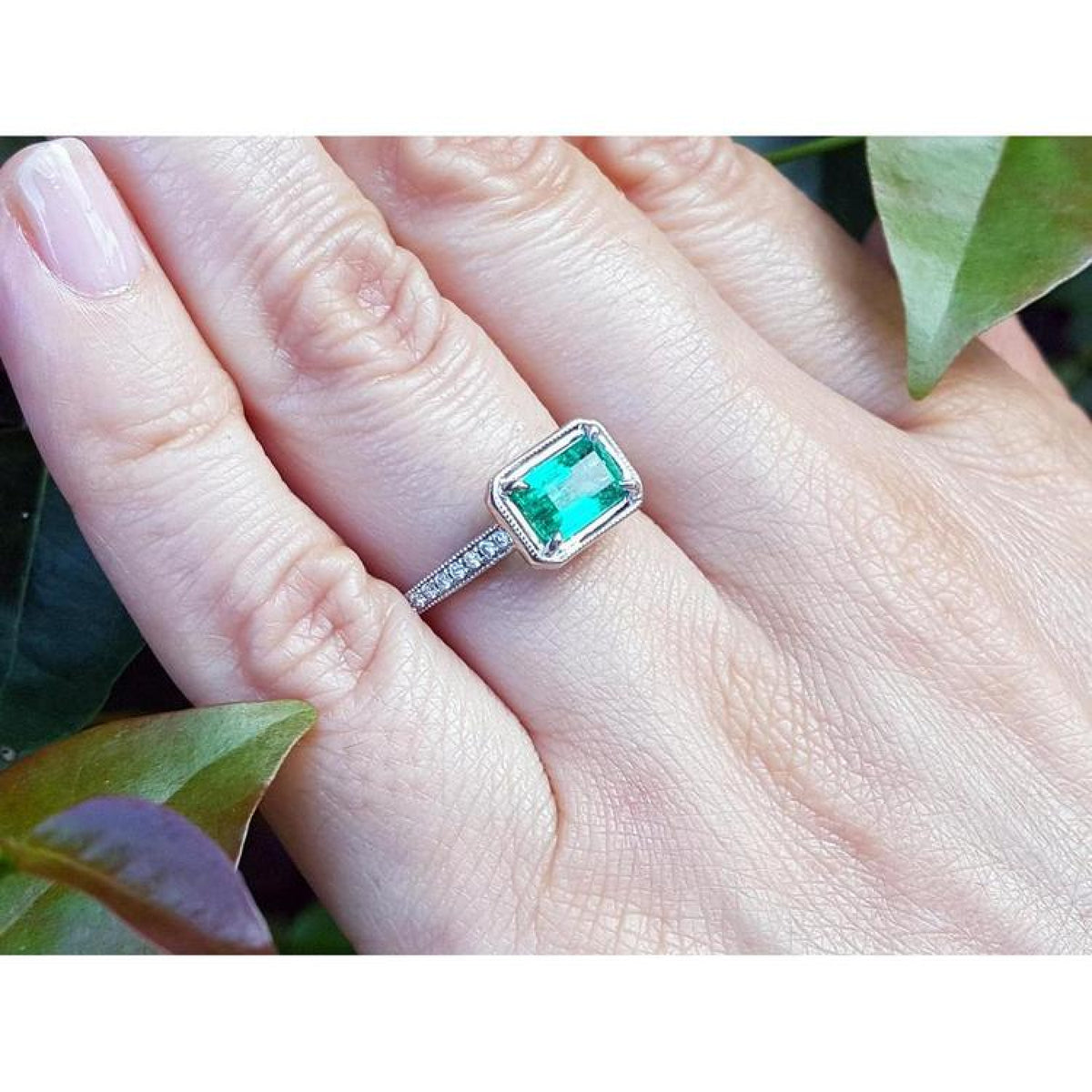 1.21 ct. emerald-cut emerald ring with natural diamonds on a 14K white gold band, worn on a hand.