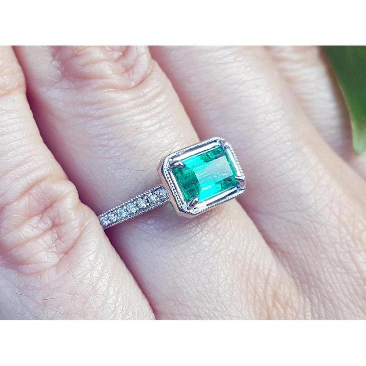1.21 ct. emerald-cut emerald ring with natural diamonds set in 14K white gold on a finger.