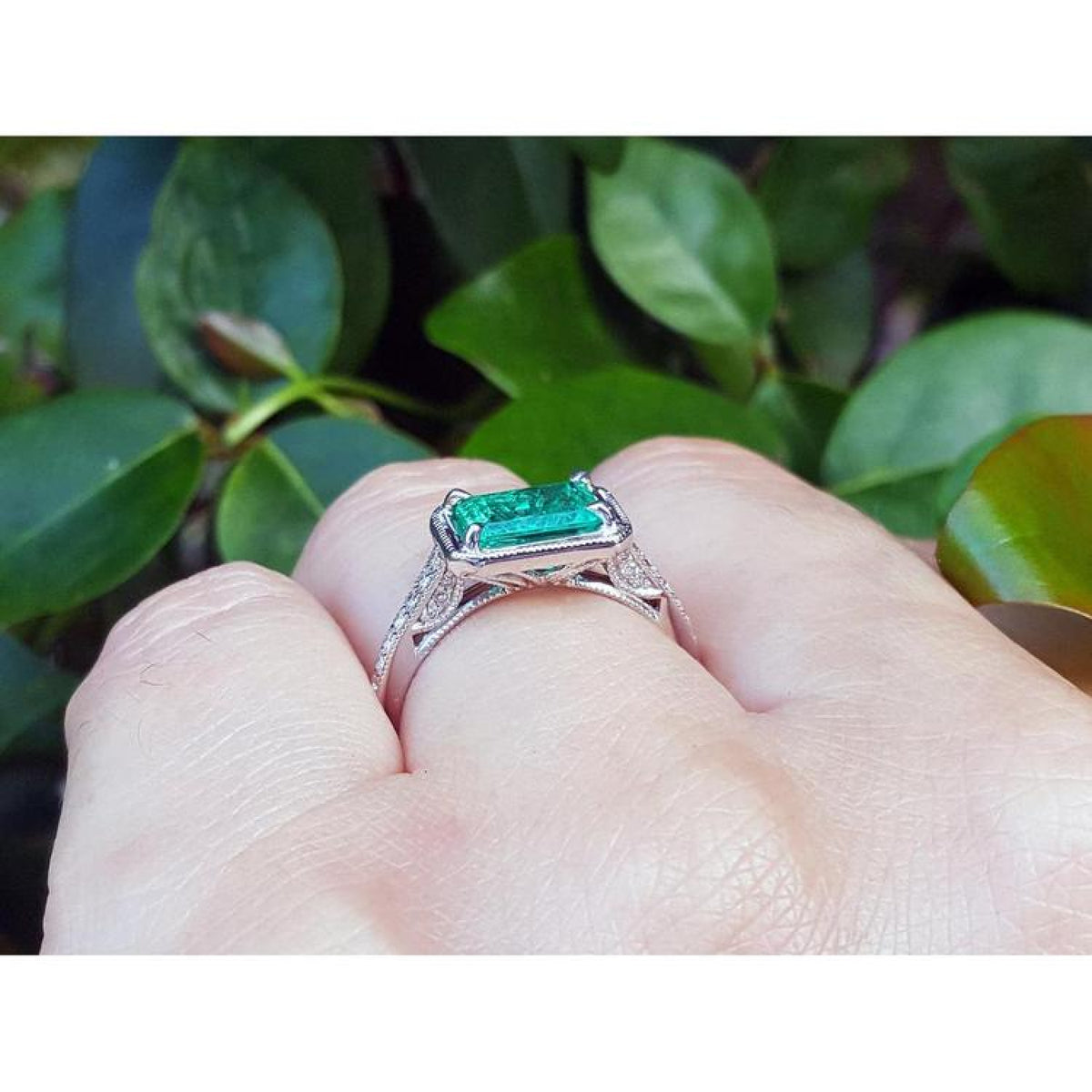 1.21 ct emerald-cut emerald ring with natural diamonds in 14K white gold on a finger.