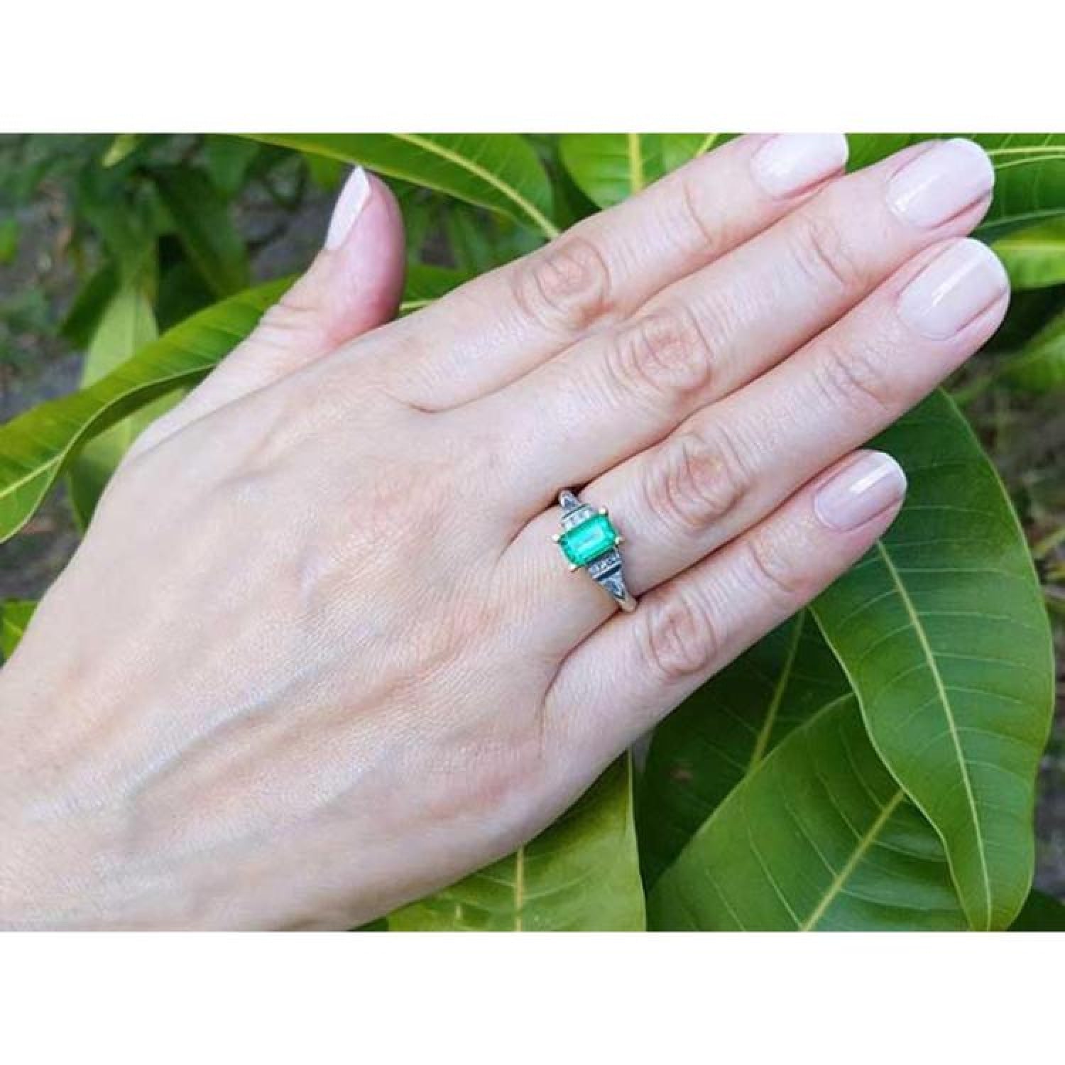 Platinum emerald ring with 18K yellow gold setting, natural round and trillion-cut diamond accents on a hand.