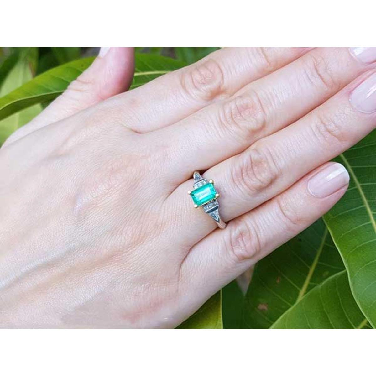 Hand wearing a ring with natural emerald against a leafy background.