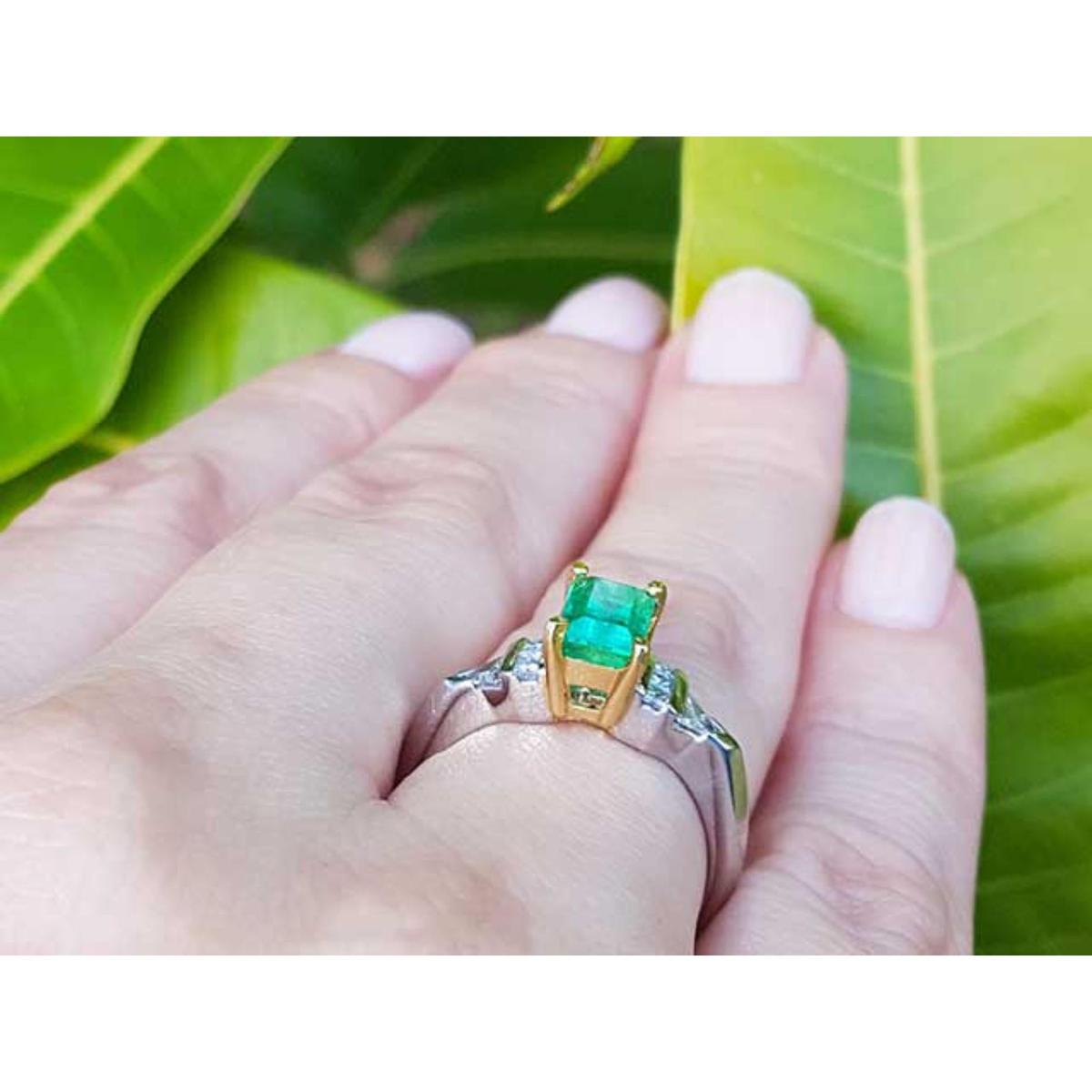 Gold and platinum ring with a natural emerald on a hand against a green leafy background.