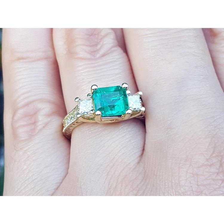 This is a women's emerald ring with princess cut side diamonds and is made of 18k yellow gold.
