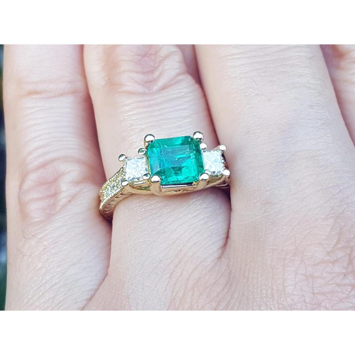 This is a women's emerald ring with princess cut side diamonds on a finger.