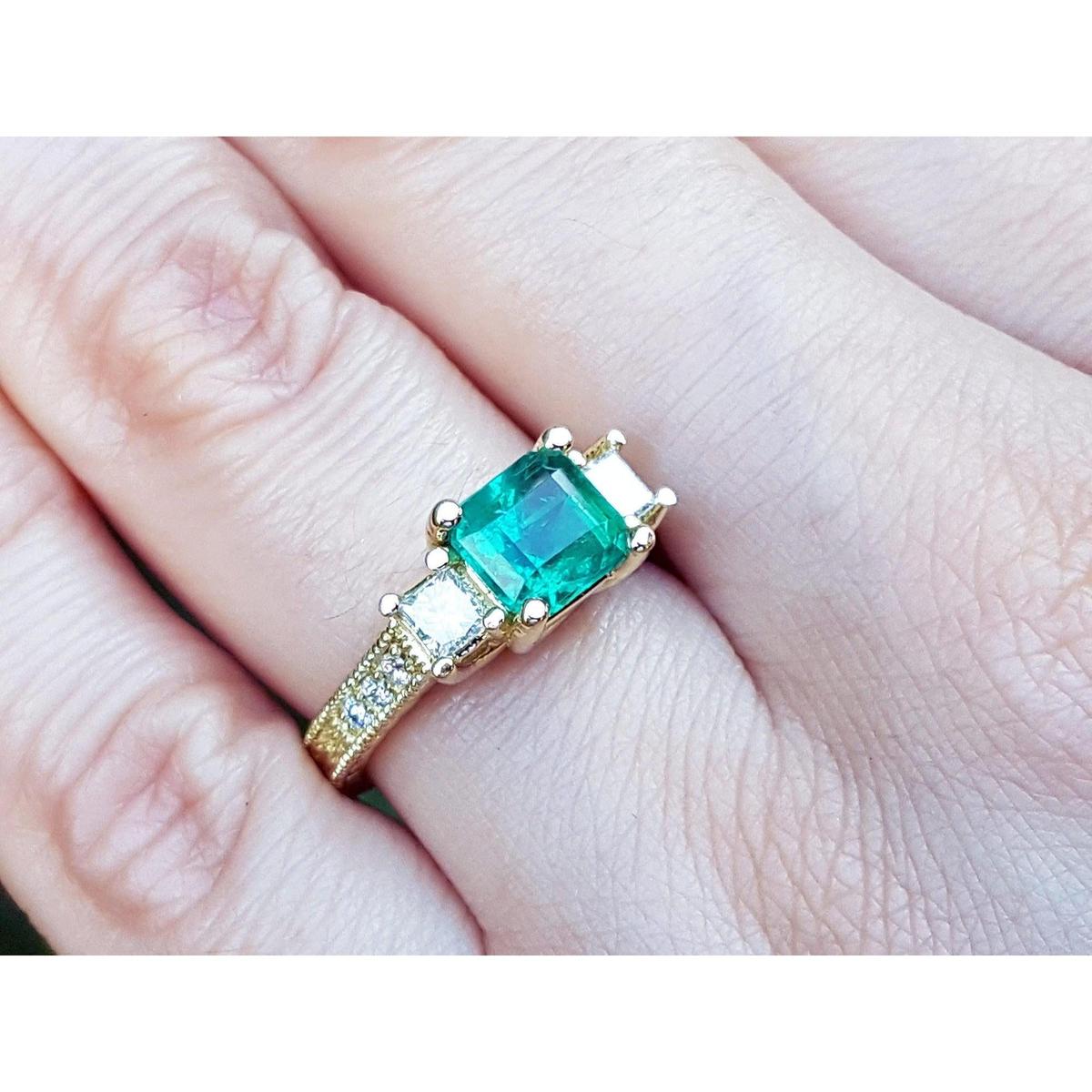 Bridal's engagement ring with emerald and side diamonds princess cut on a finger.