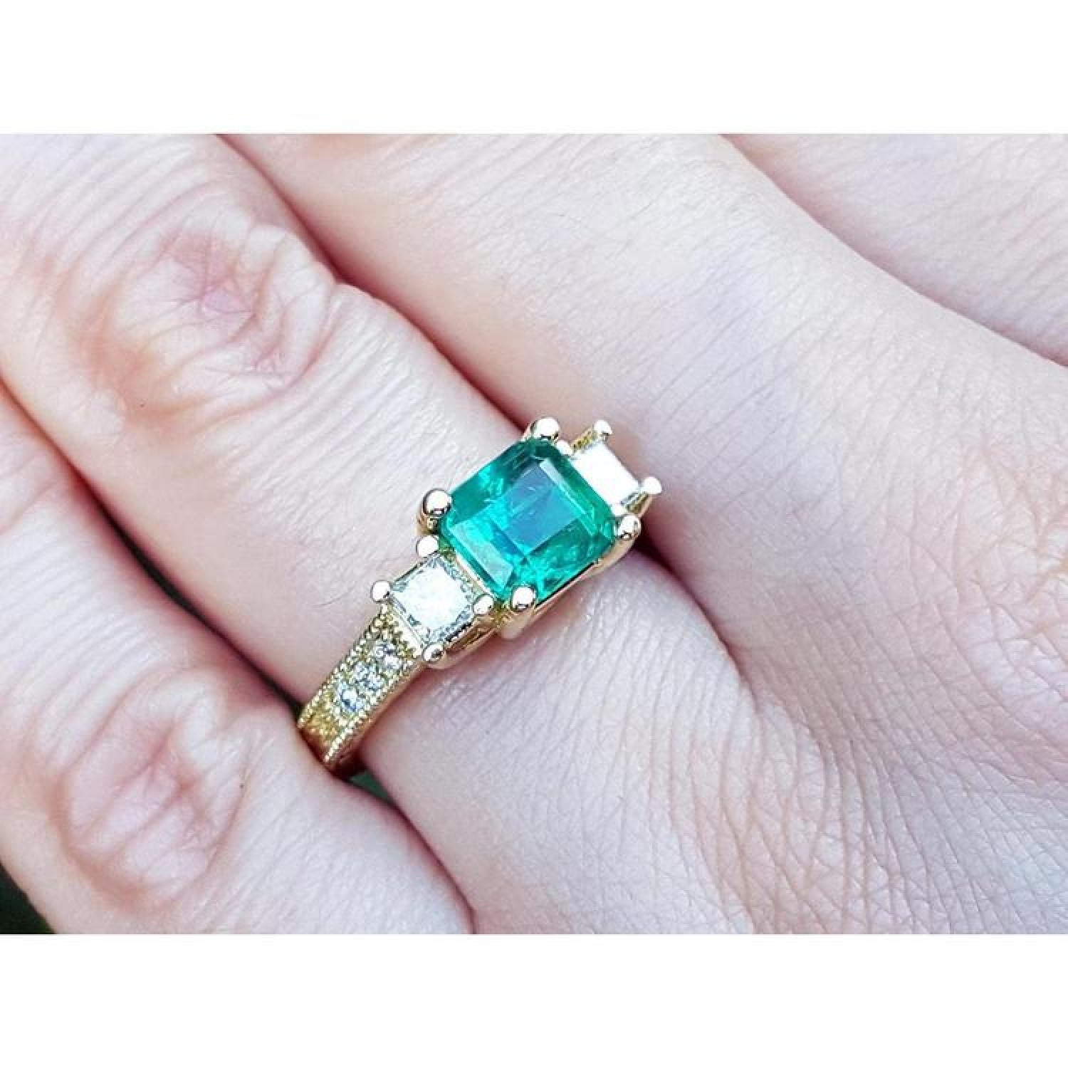 Yellow gold ring with a large emerald cut emerald and two princess cut side diamonds.