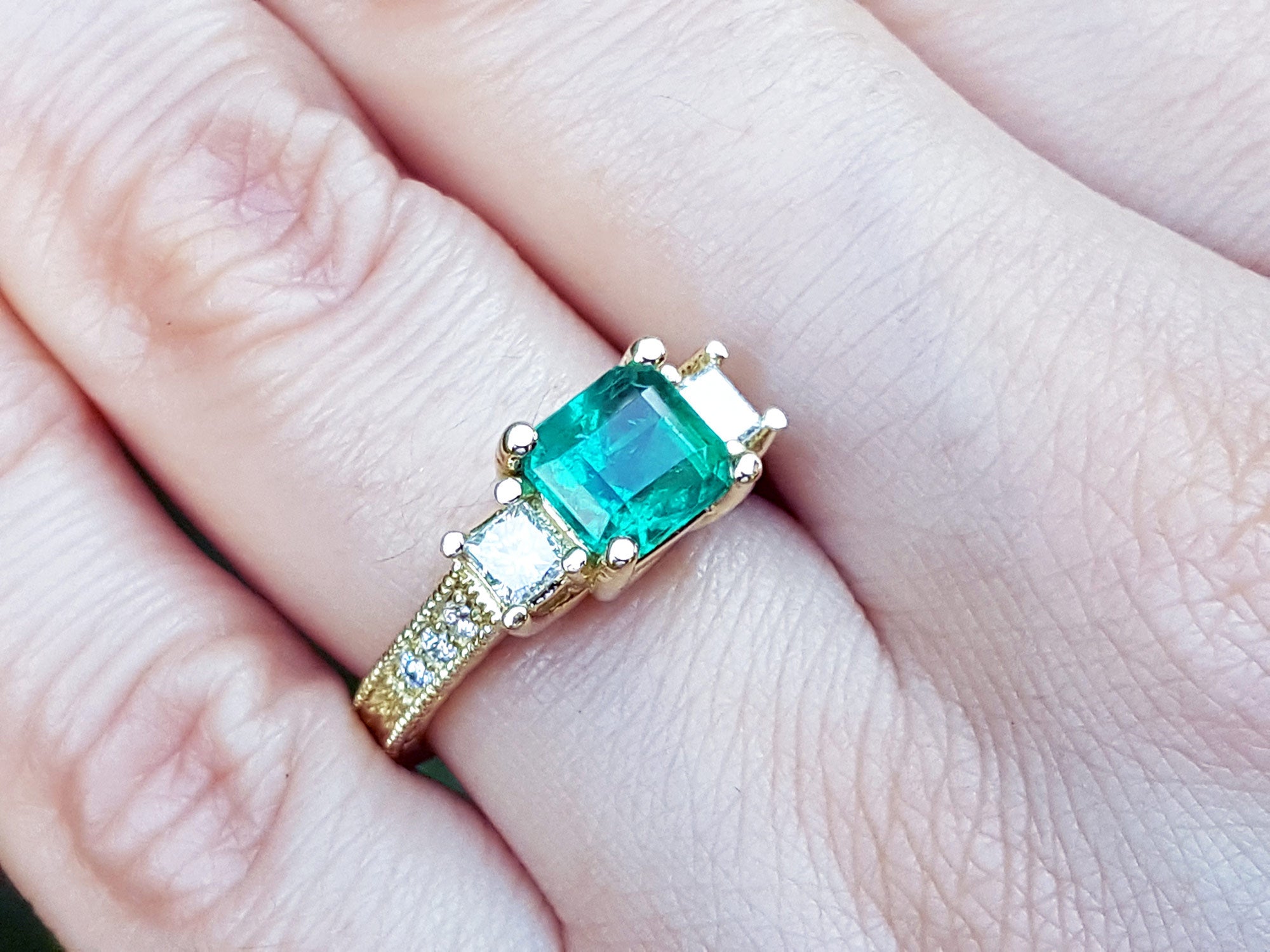 Bridal&#39;s engagement ring with emerald and side diamonds princess cut on a finger.