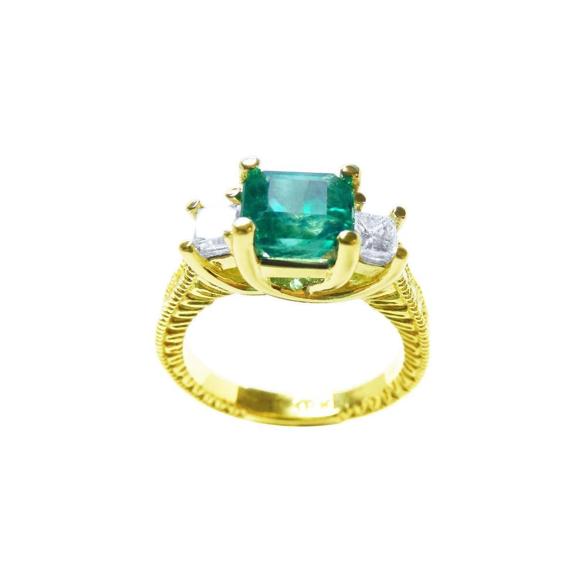 A 18k yellow gold emerald ring with side princess cut diamonds, on a white background.