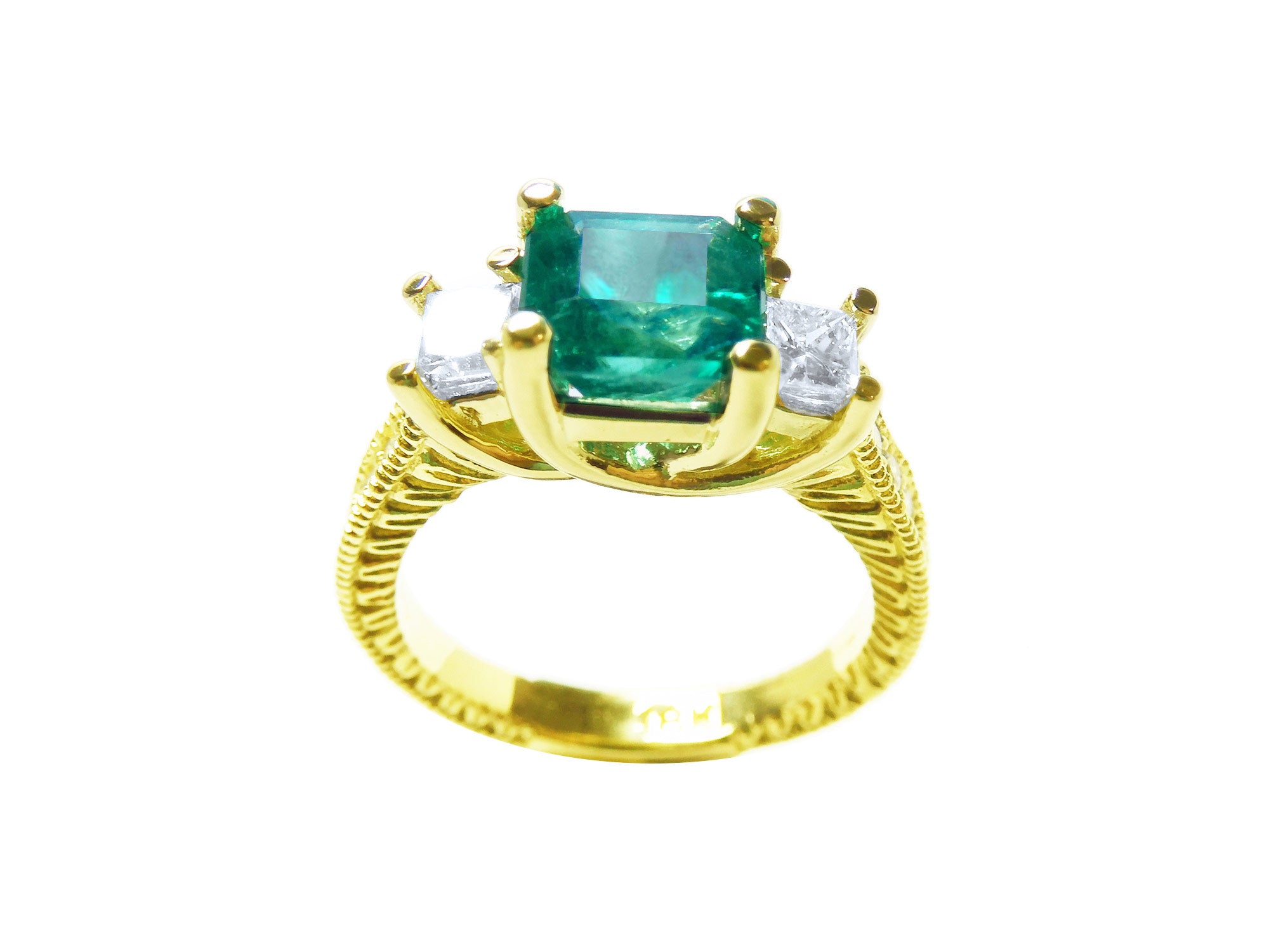 A 18k yellow gold emerald ring with side princess cut diamonds, on a white background.
