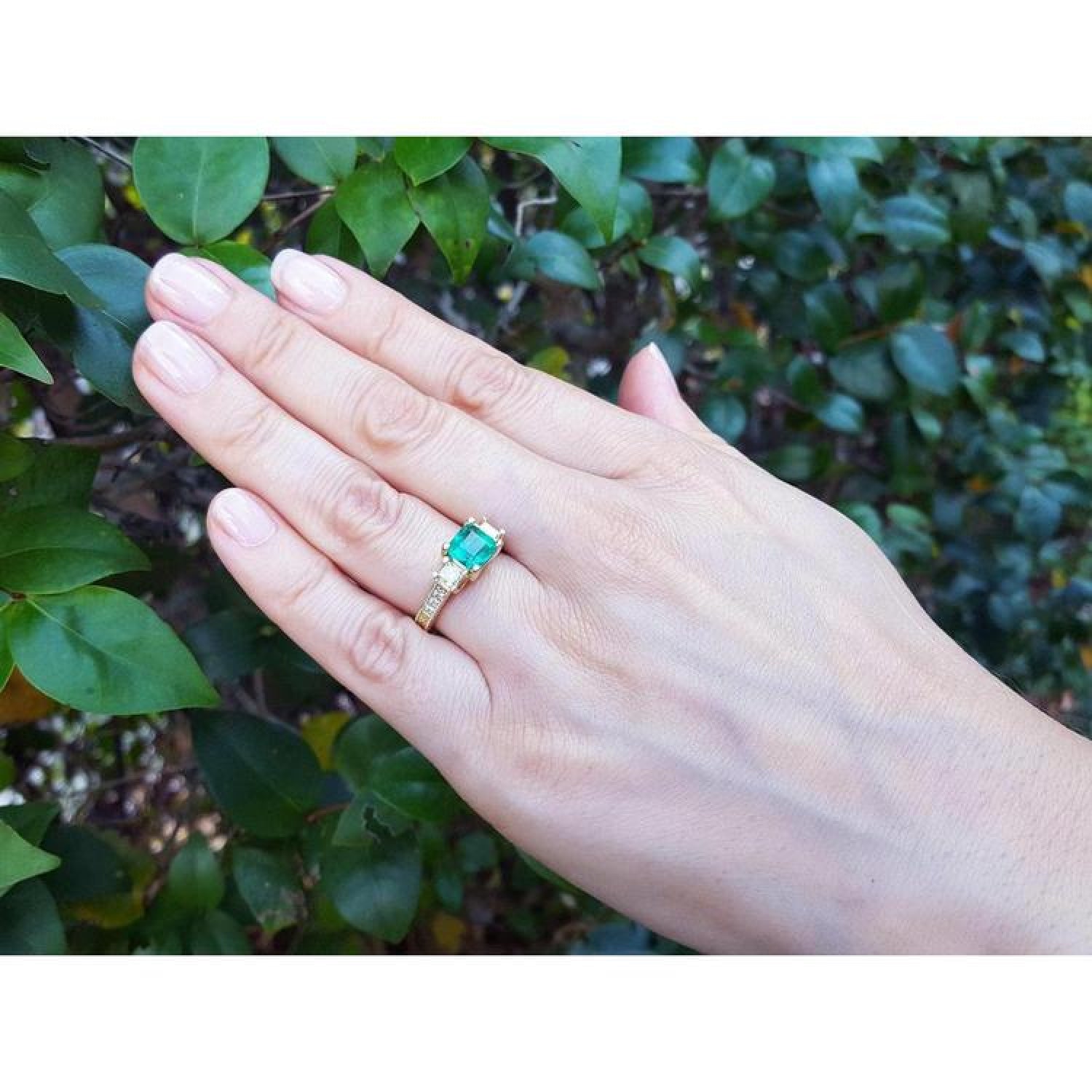 Yellow gold 18K ring with emerald and princess cut side diamonds on a hand.