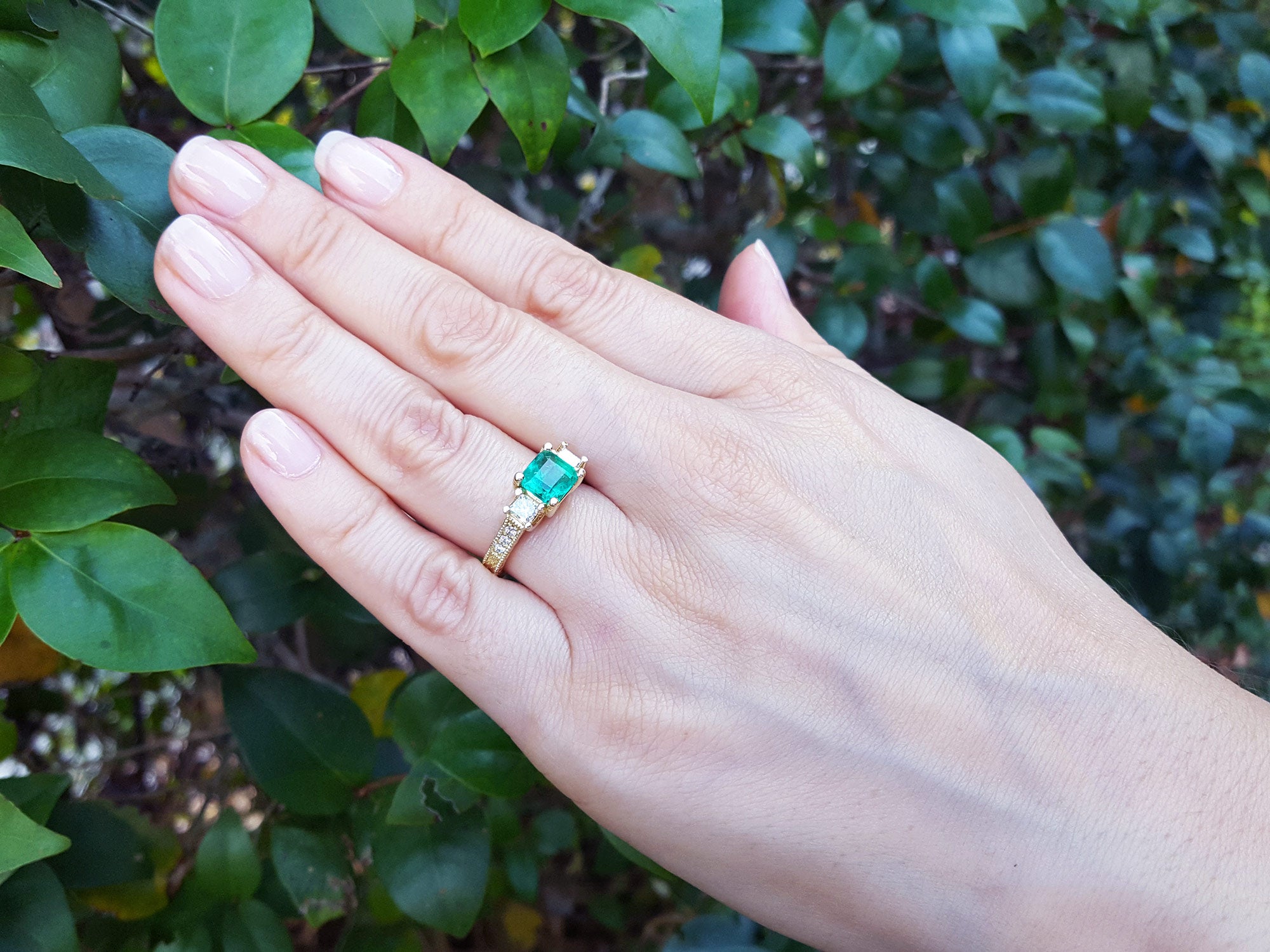 Hand wearing a May&#39;s birthstone ring for women against a leafy background