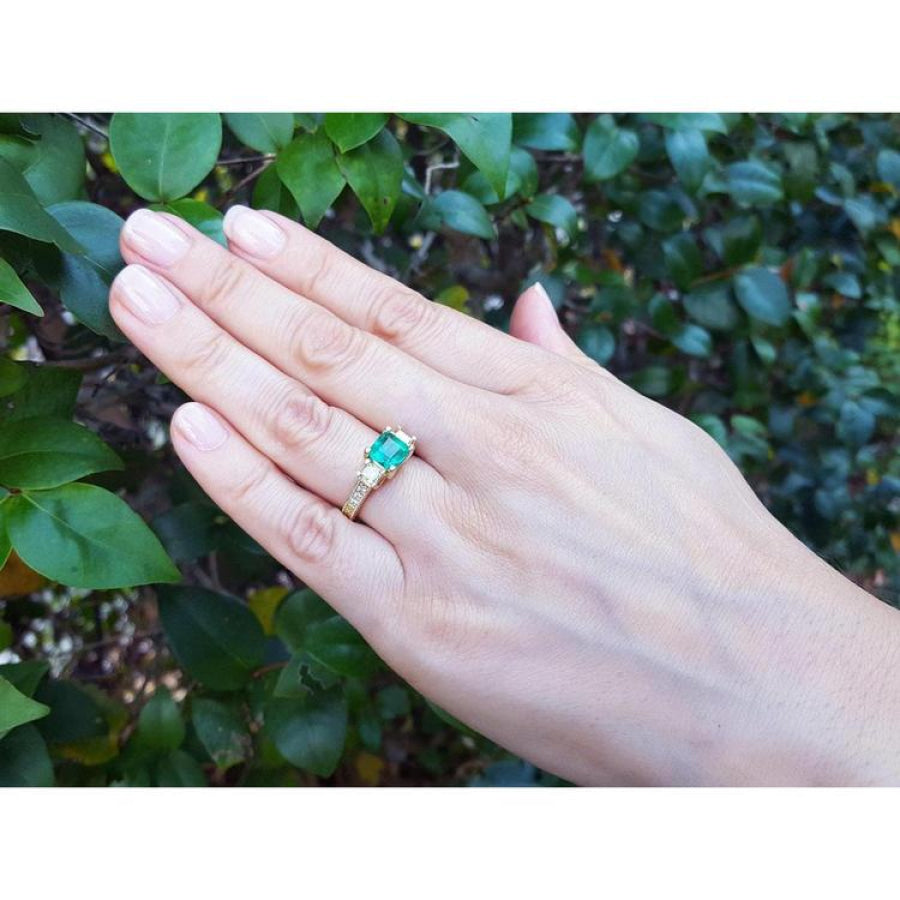 Yellow gold 18K ring with emerald and princess cut side diamonds on a hand.