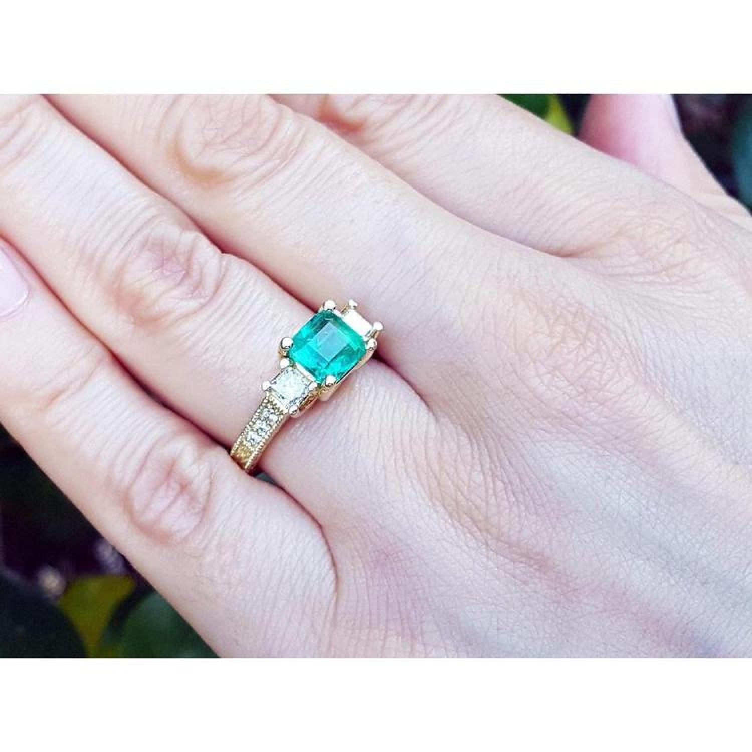 Emerald and princess cut side diamond ring in 18K yellow gold with antique decor on a hand.