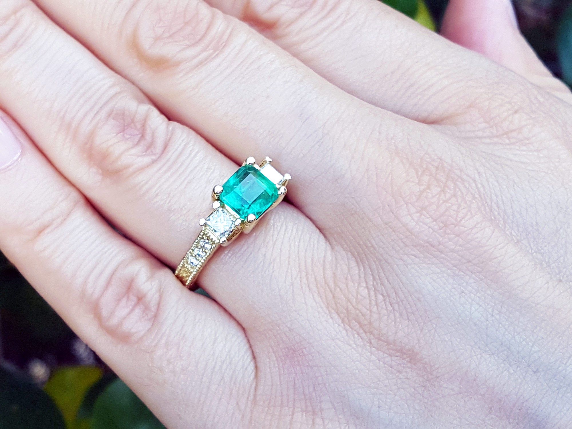 A Mother&#39;s Day gift emerald and side princess cut diamonds ring on a person&#39;s finger.