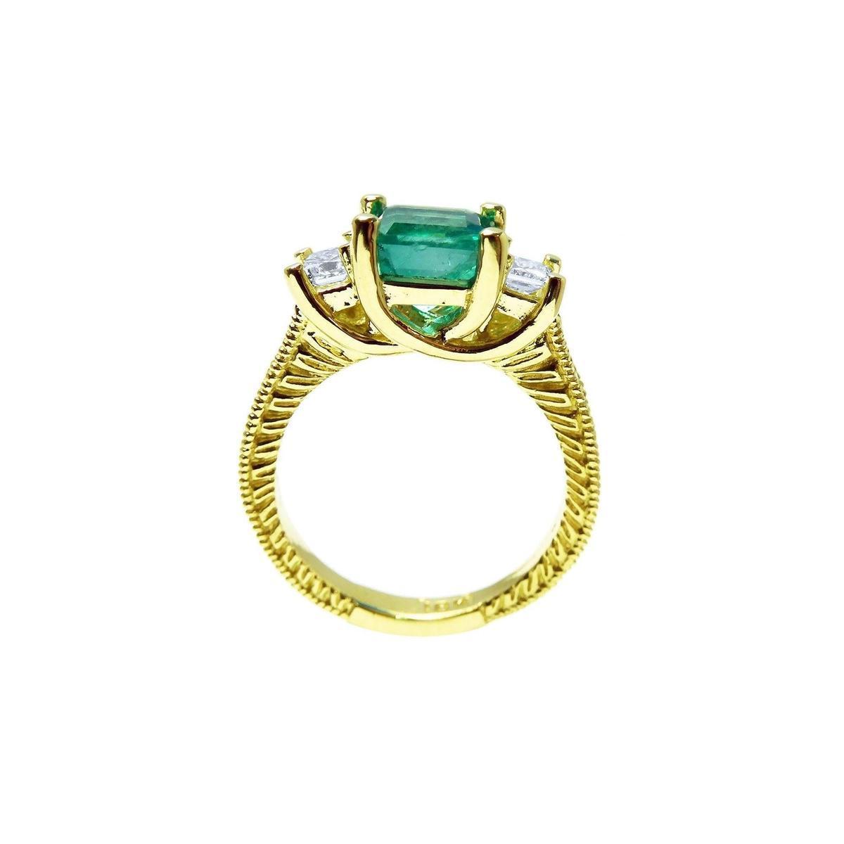 A lateral profile view including gallery of an emerald ring with side princess cut diamonds in 18k yellow gold.