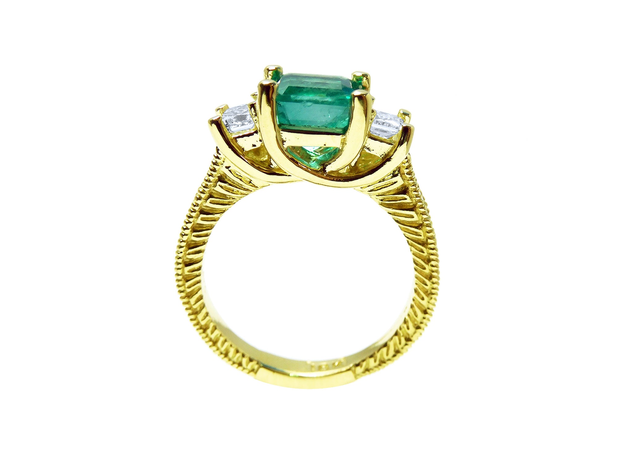 A lateral profile view including gallery of an emerald ring with side princess cut diamonds in 18k yellow gold.