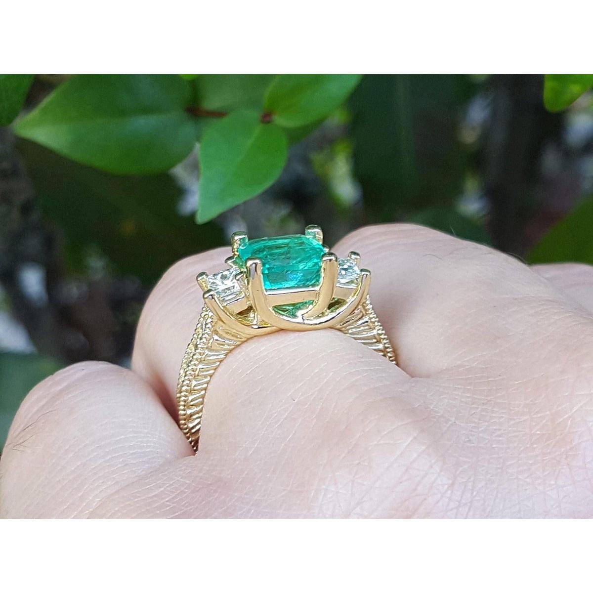 A Brial's may birthstone emerald ring held in a hand against a blurred green leafy background.
