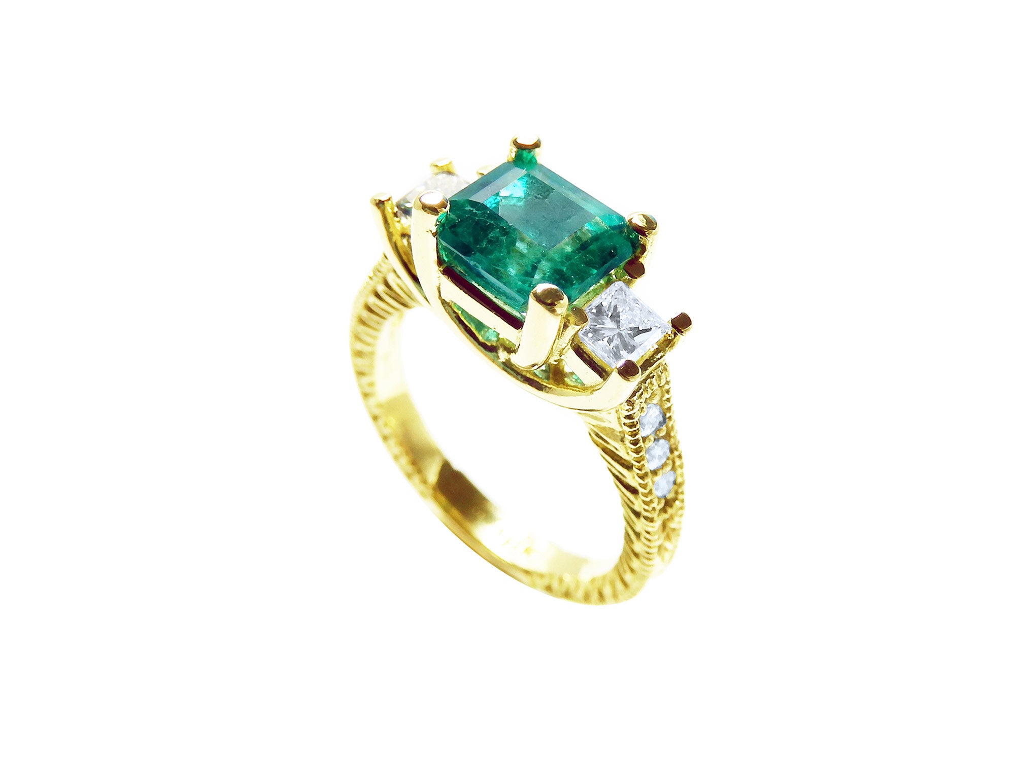 An emerald ring with side princess cut diamonds on a white background.