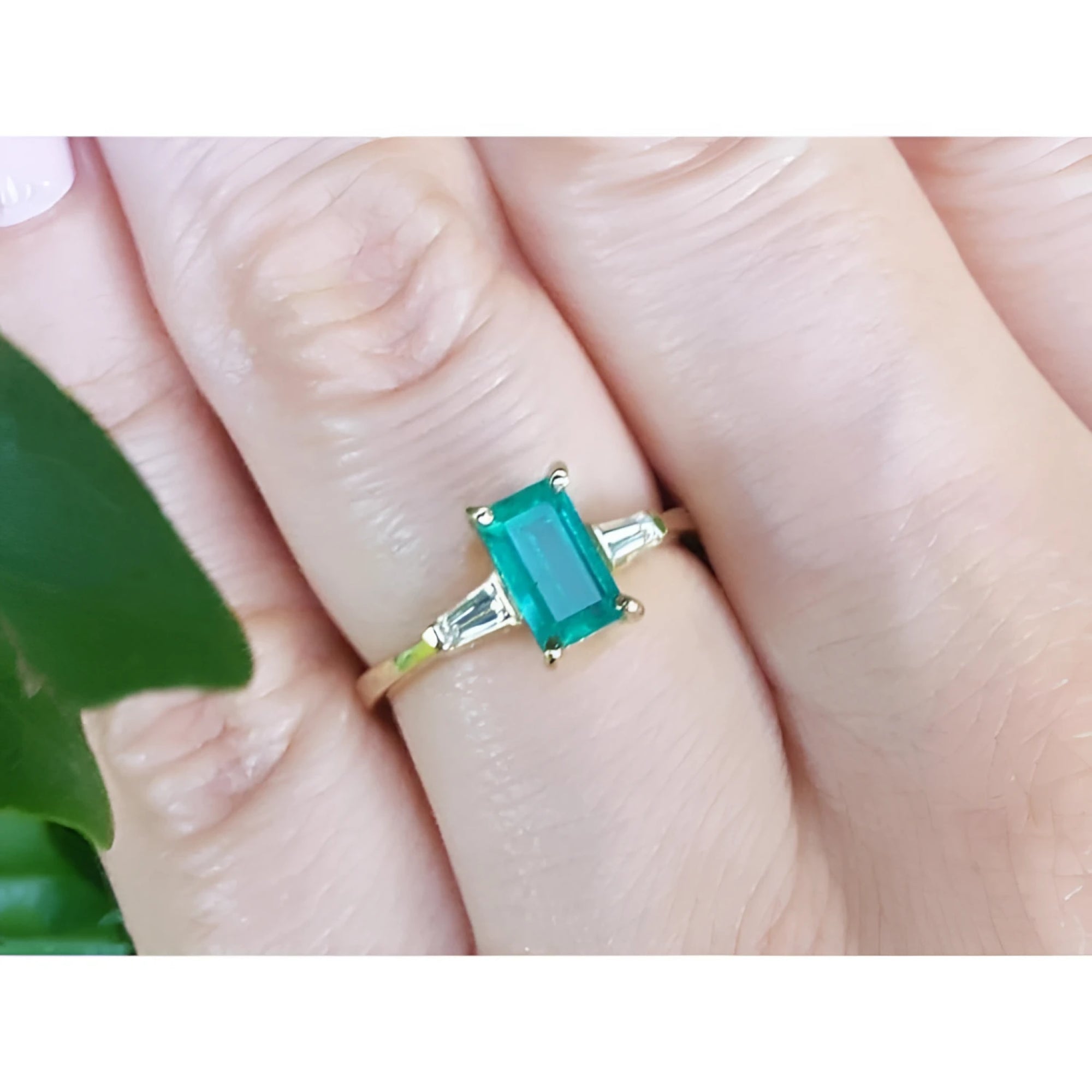 A natural colombian emerald and side baguette diamonds ring for women on a finger.