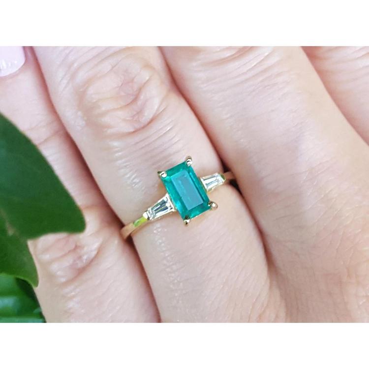 A natural colombian emerald and side baguette diamonds ring for women on a finger.