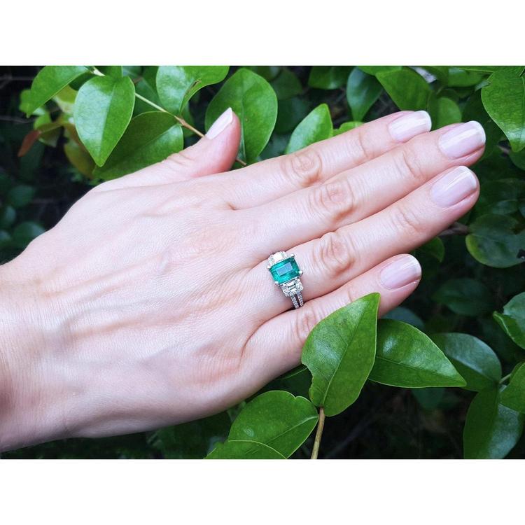 Emerald ring with side emerald-cut and round diamonds in 18k white gold on a hand.