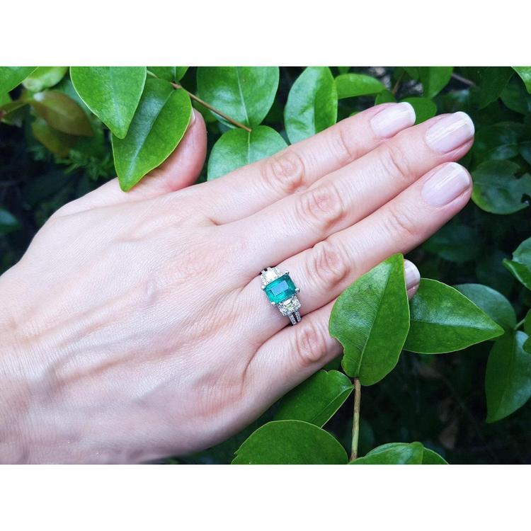 1.88 carat emerald ring with side emerald-cut and round diamonds in 18k white gold on a hand.