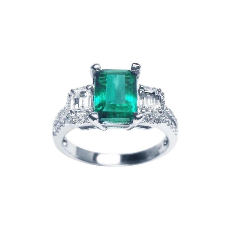 A tree stone emerald engagement ring with side emerald-cut natural side diamonds made of 18k white gold.