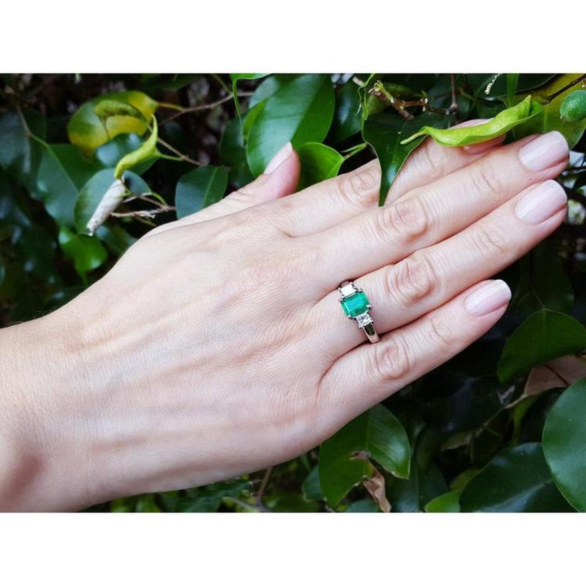18k white gold three stone ring with a 1.38 ct emerald and two princess cut diamonds on a hand.