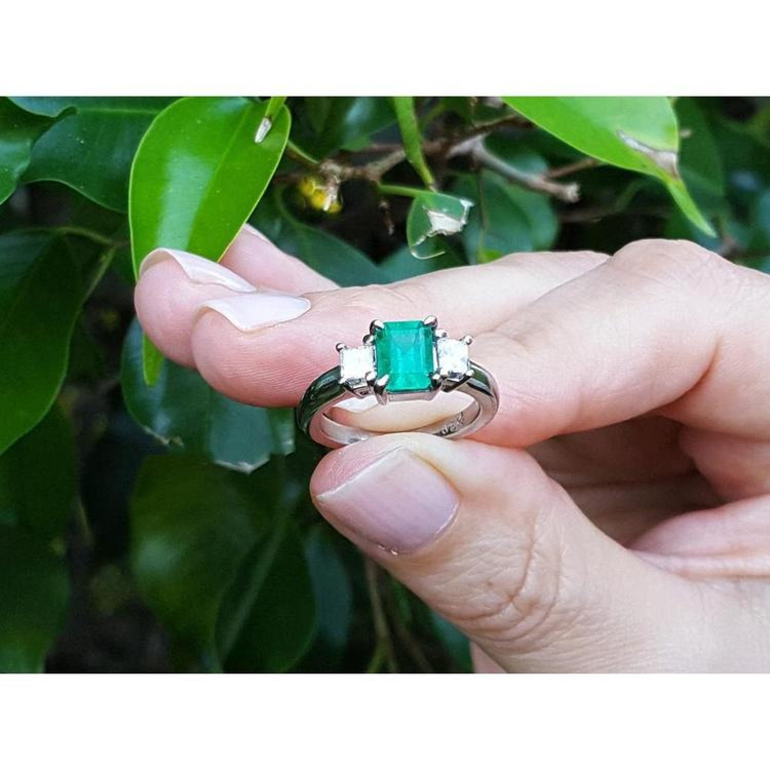 18k white gold three-stone ring with a vibrant emerald and two princess-cut side diamonds.