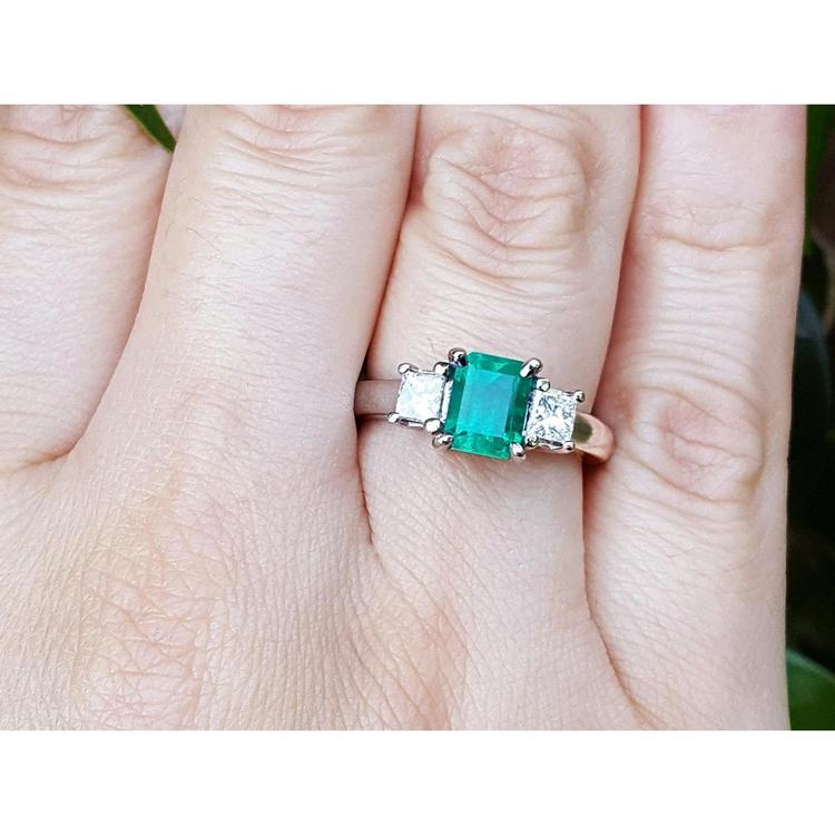 This three stone natural colombian emerald ring with side princess cut diamonds is on a finger.