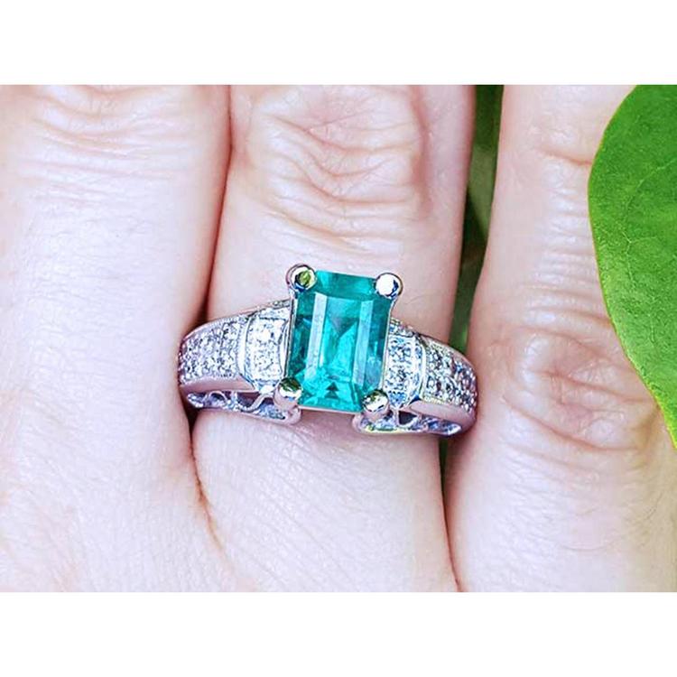 A women's Colombian emerald ring in 18k white gold and accent diamonds on a finger.