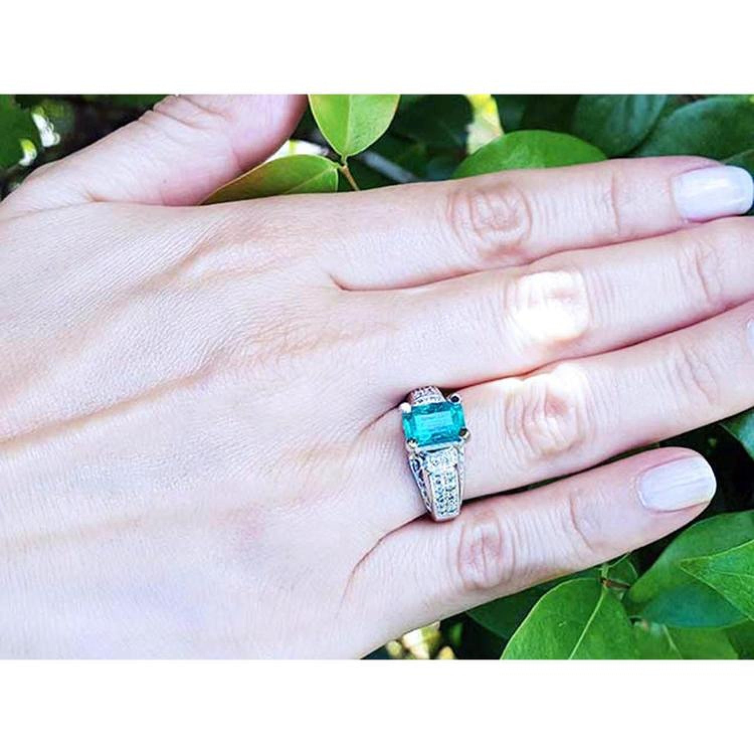 Emerald-cut emerald ring for women in 18K white gold with diamond accents on a hand.