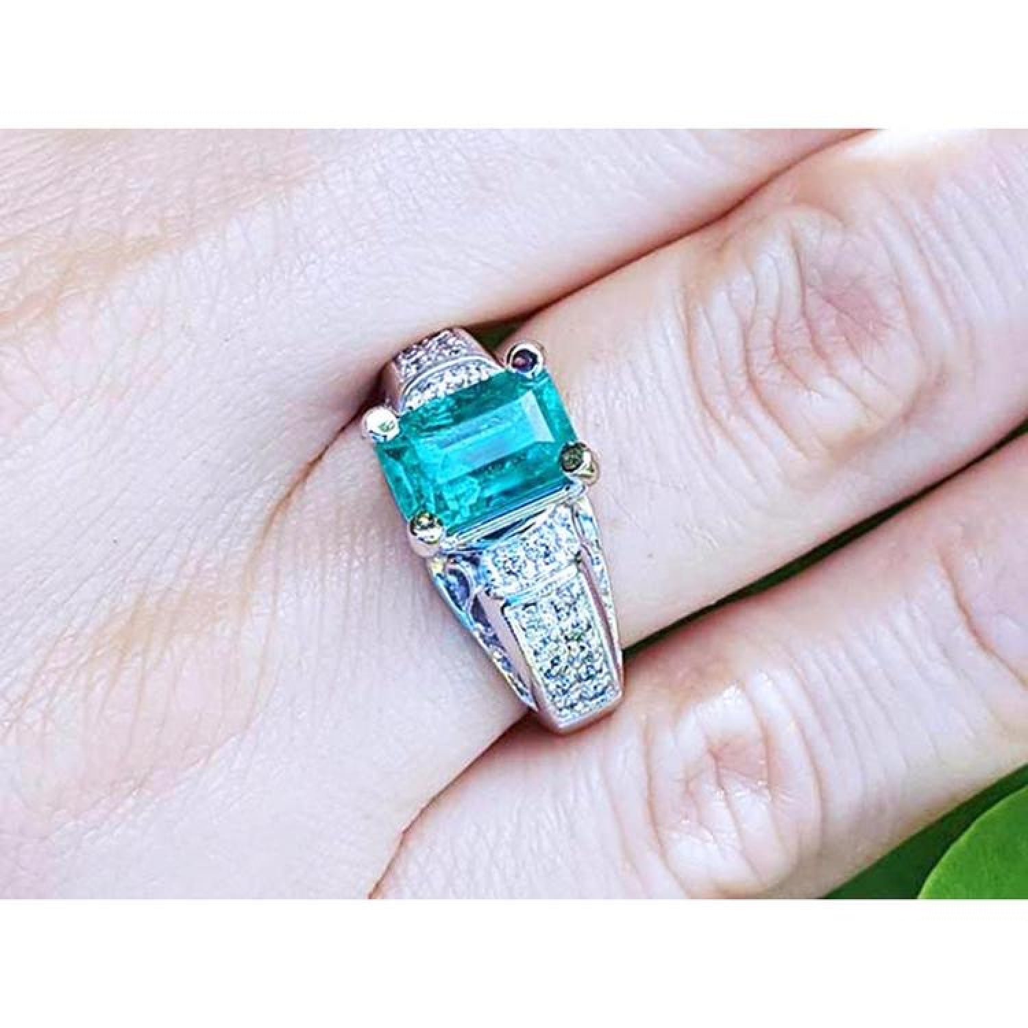 Emerald-cut 2.02 ct. Colombian emerald ring with diamonds in 18K white gold on a finger.
