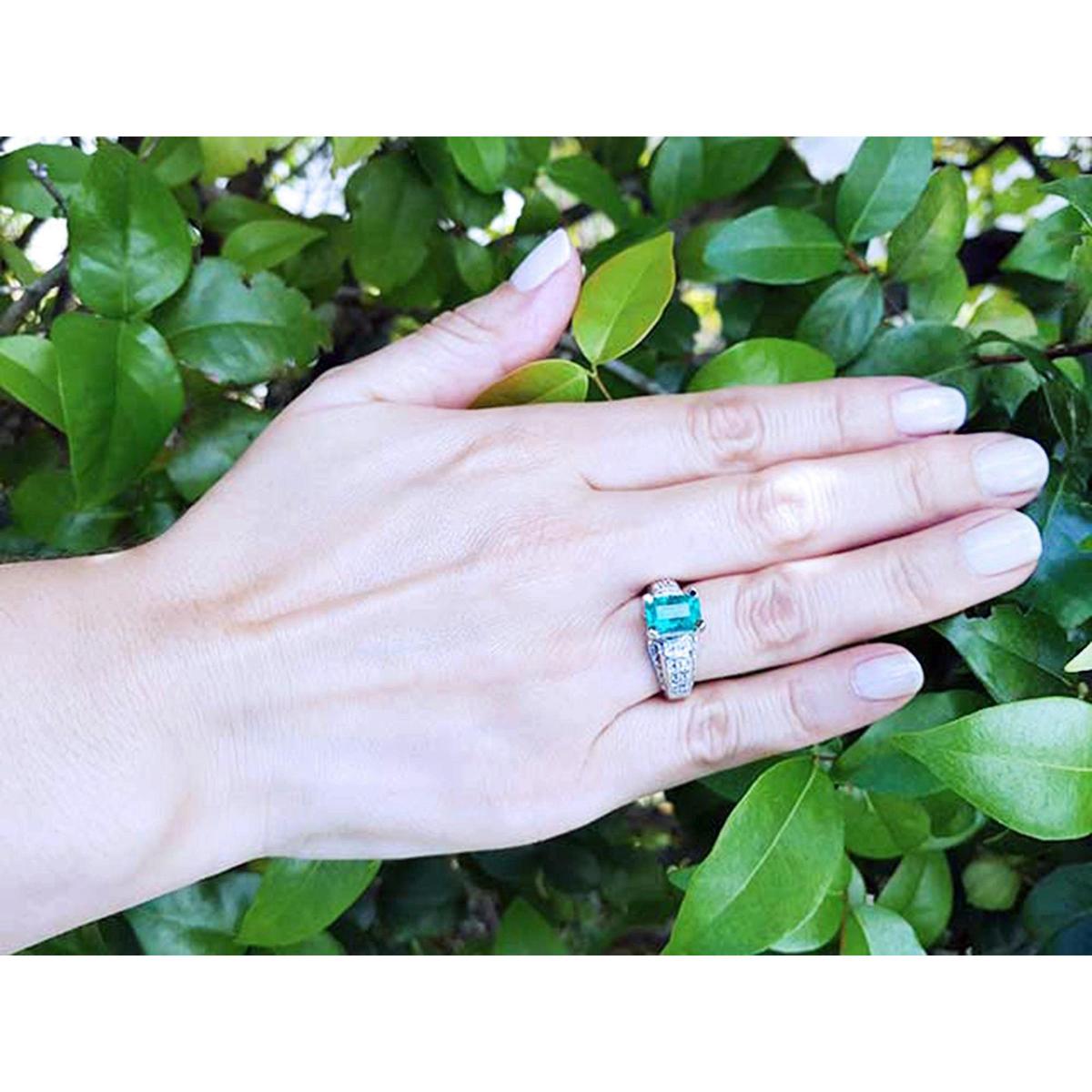 Hand wearing a ring with a natural Colombian emerald against a green leafy background.