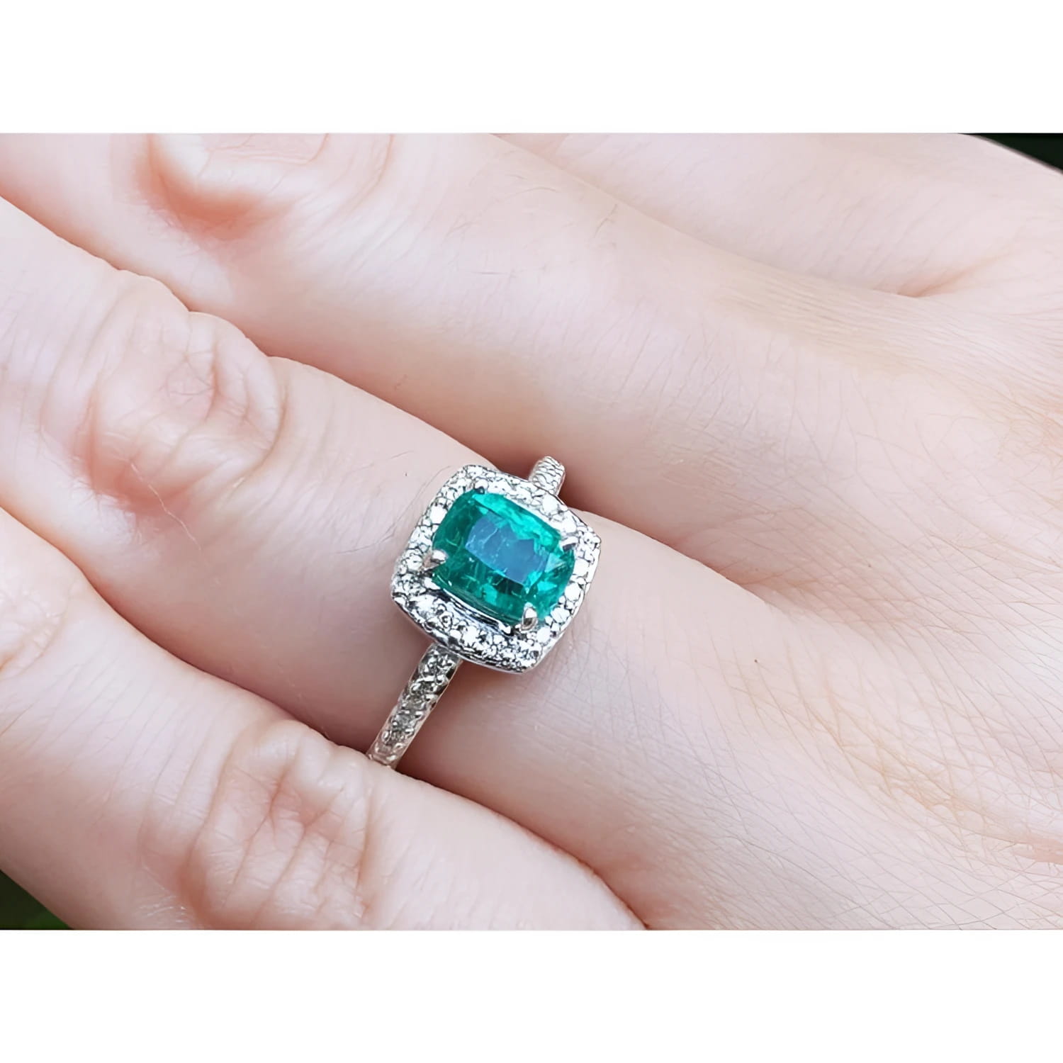Women's 1.19 ct cushion cut emerald ring with diamond halo, set in 14K white gold on a finger.