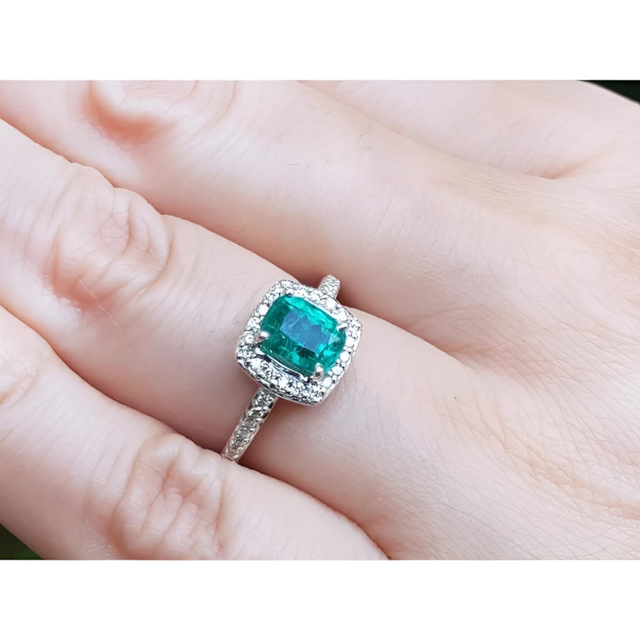 Women's 1.19 ct cushion cut emerald ring with diamond halo, set in 14K white gold on a finger.
