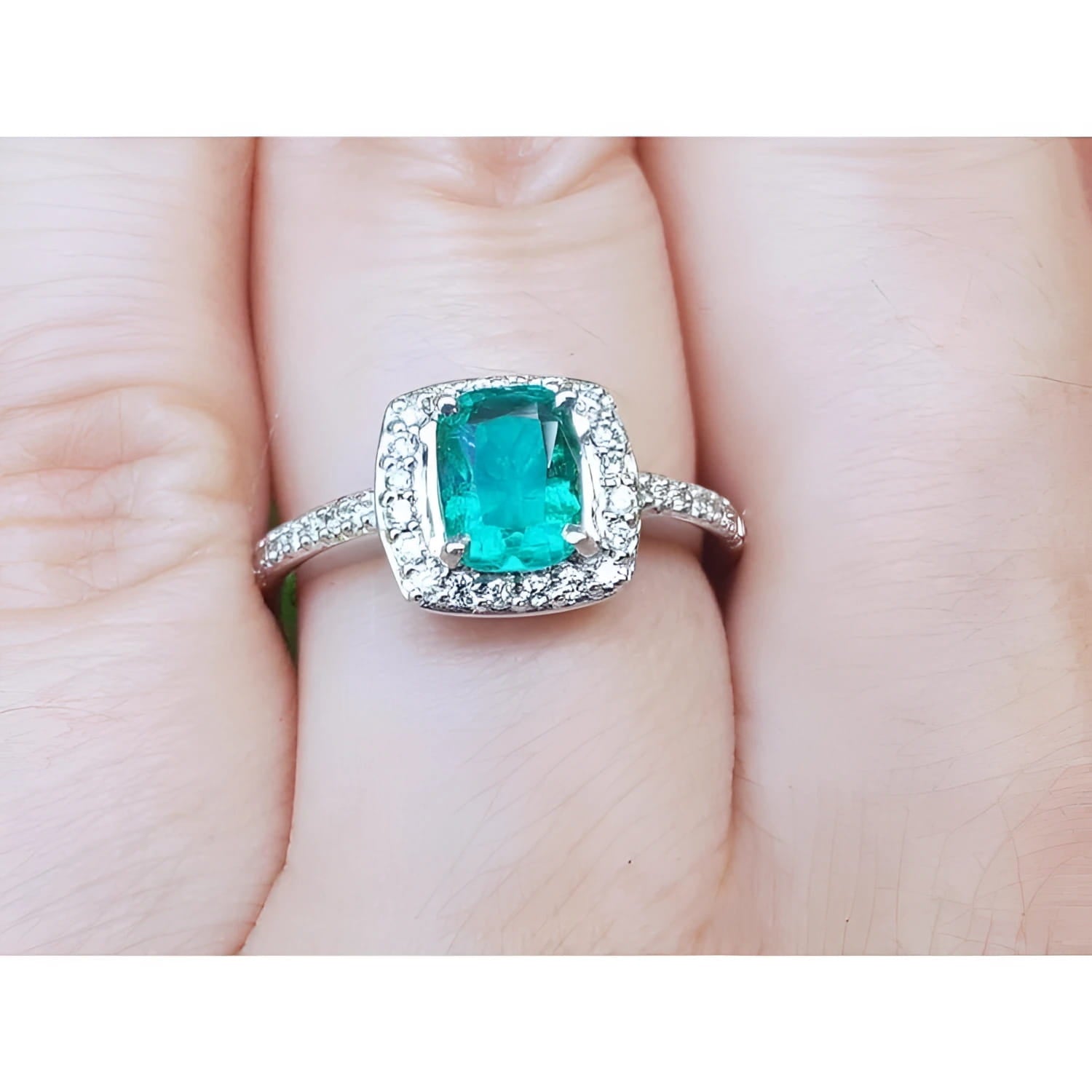 A women's emerald ring cushion cut with halo of natural diamond in white gold on a finger.