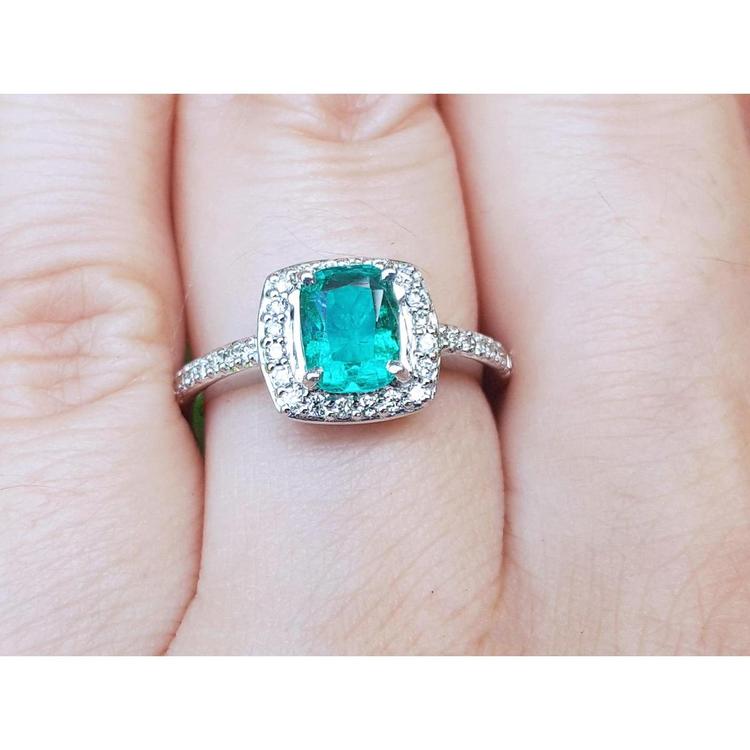 A women's emerald ring cushion cut with halo of natural diamond in white gold on a finger.