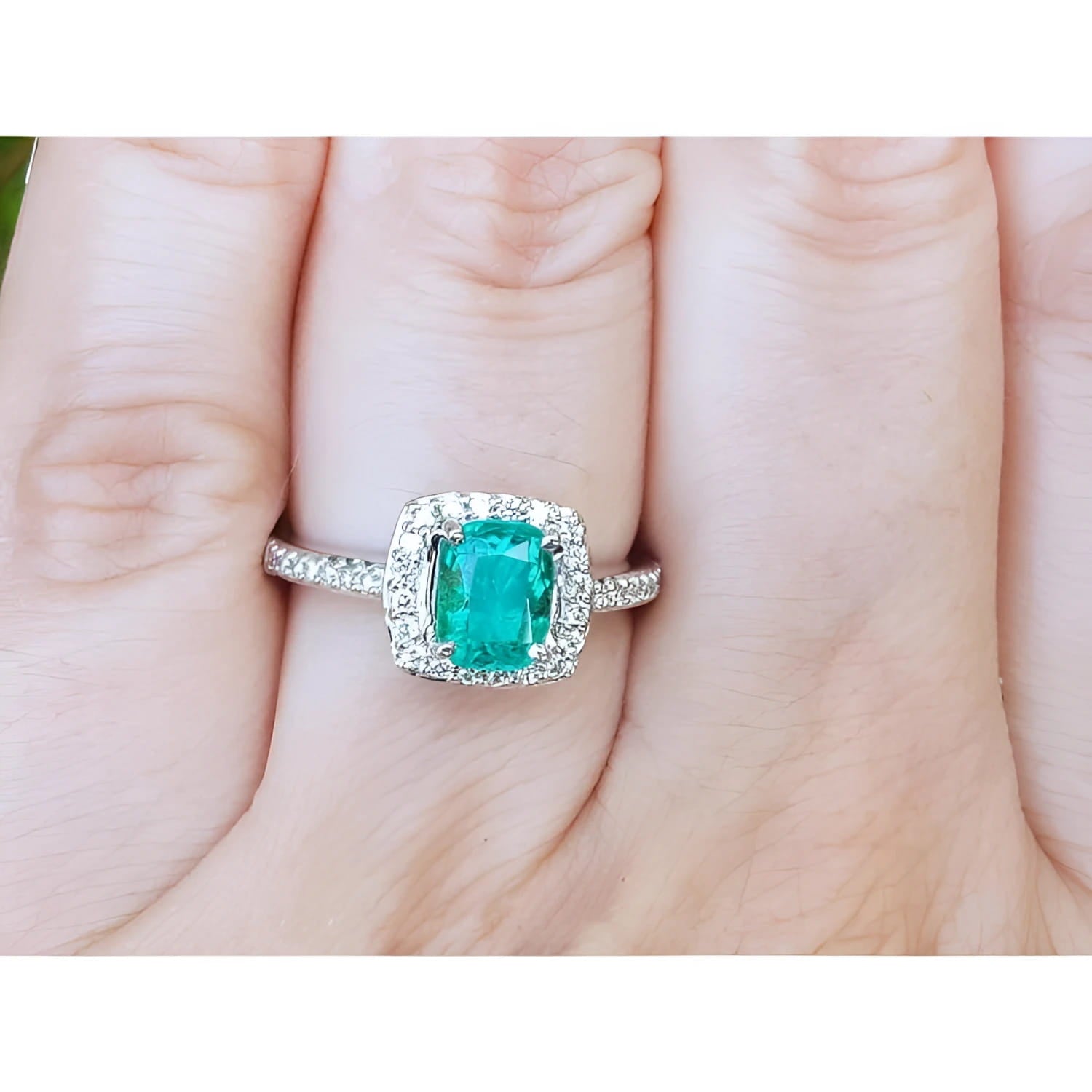Women's cushion cut emerald ring with diamond halo and band in 14K white gold.